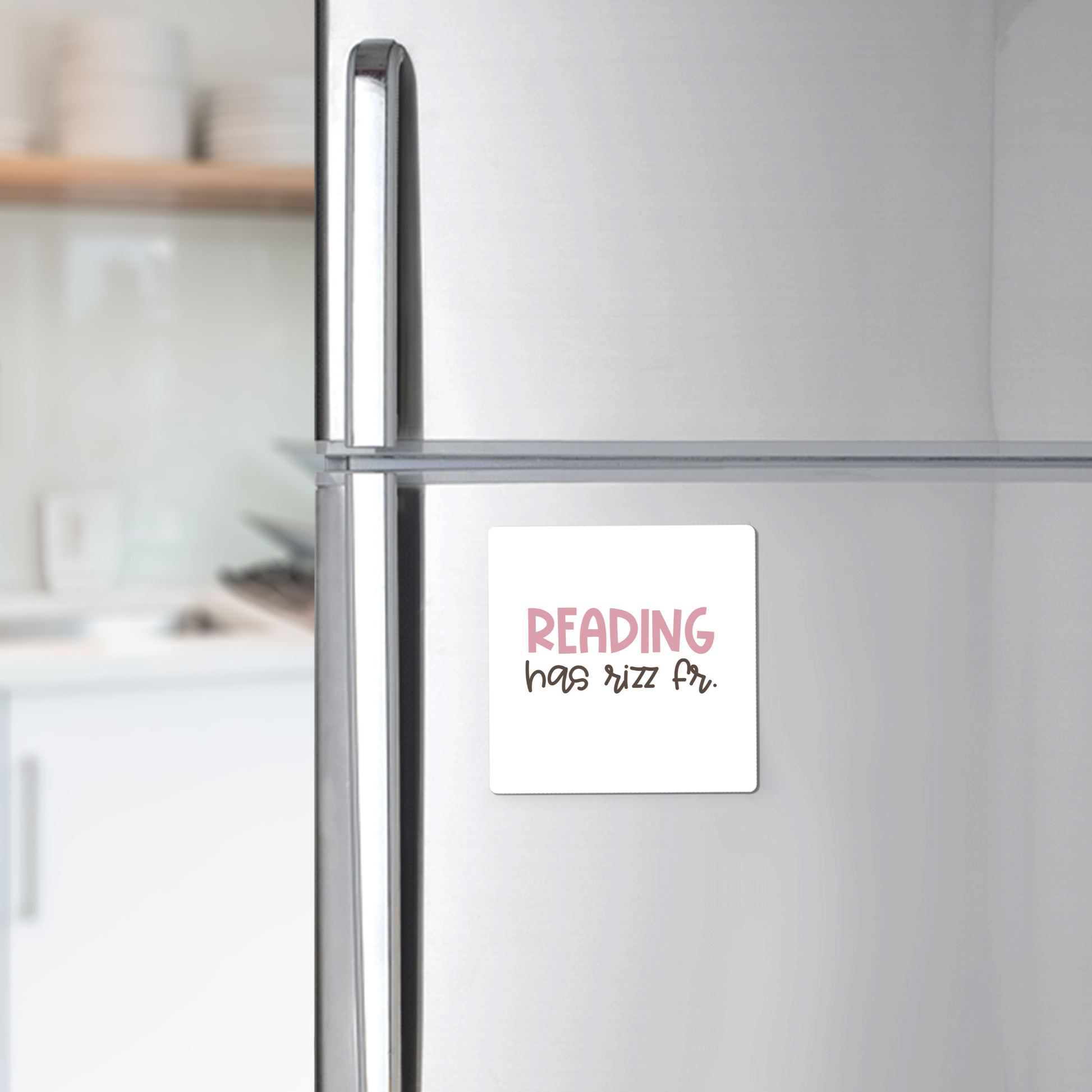 A modern kitchen features a silver refrigerator with the Mirabilia Boutique "Reading Has Rizz Fr Magnet"—a playful teacher gift or classroom decor displaying “READING has rizz fr.” in pink and black.