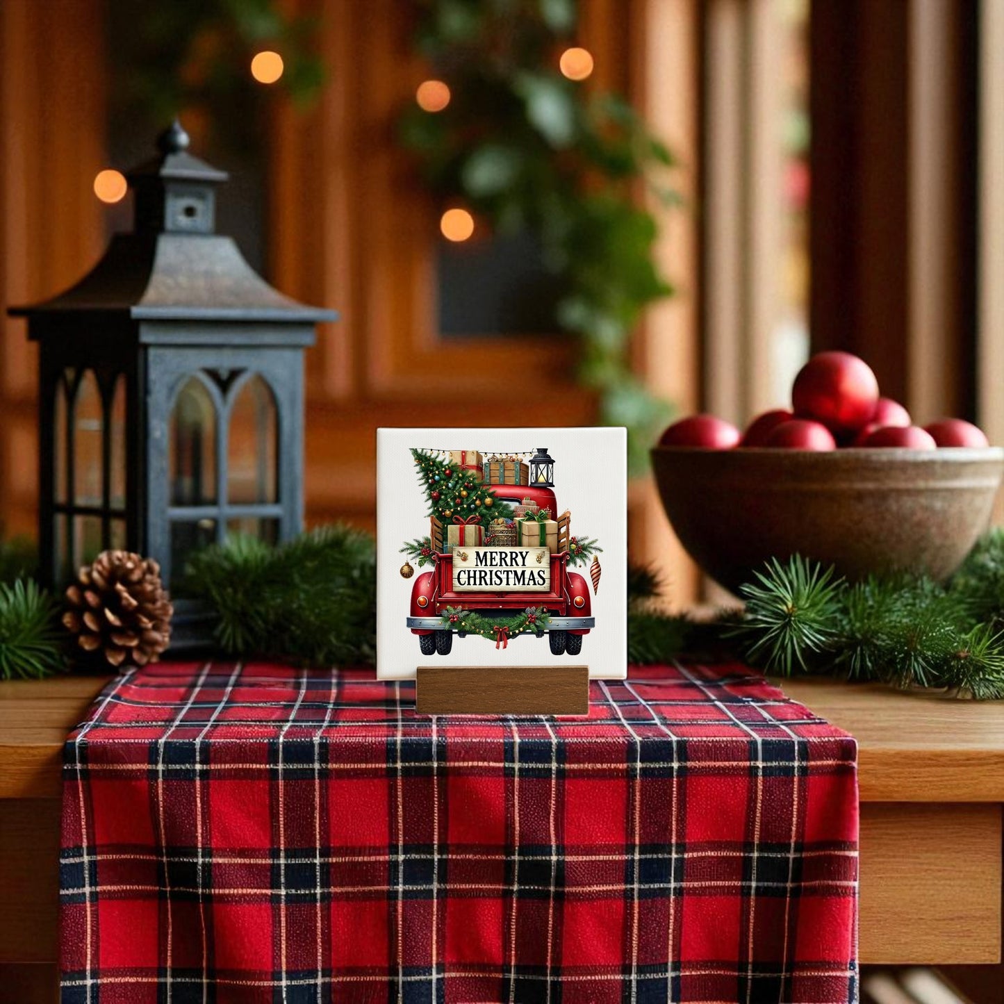 A festive table showcases a red plaid cloth, rustic holiday decor by Mirabilia Boutique, a black lantern, pinecones, evergreens, and their Red Merry Christmas Truck Mini Sign featuring a red truck with tree & gifts. Red ornaments fill a bowl.