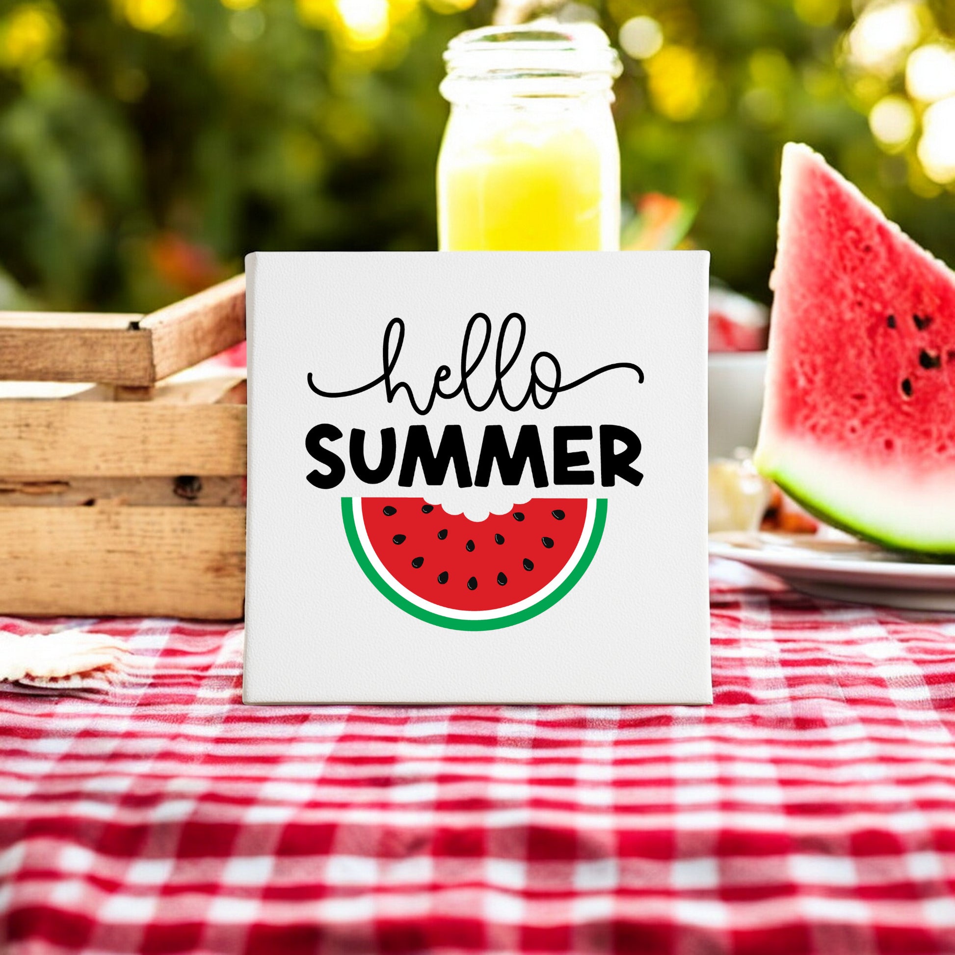The Mirabilia Boutique Hello Summer Watermelon Canvas Sign – 8x8 Fruit Wall Art sits on a red checkered cloth beside a watermelon slice, yellow drink in a mason jar, wooden crate, and greenery for vibrant summer decor vibes.