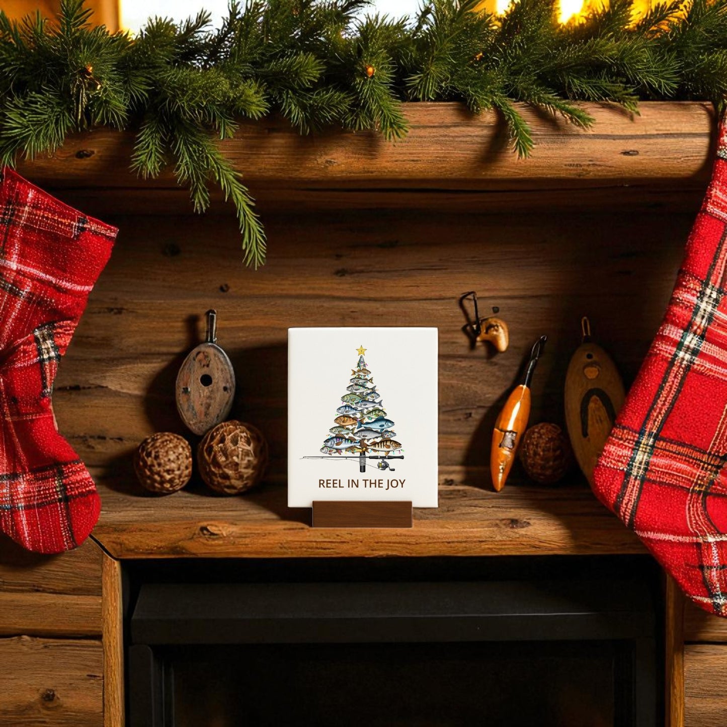 A holiday mantel decorated with evergreen branches, two red plaid stockings, fishing lures, festive balls, and the Mirabilia Boutique Fishing Christmas Sign—"Reel in the Joy" canvas decor—celebrates a love of fishing for the holidays.