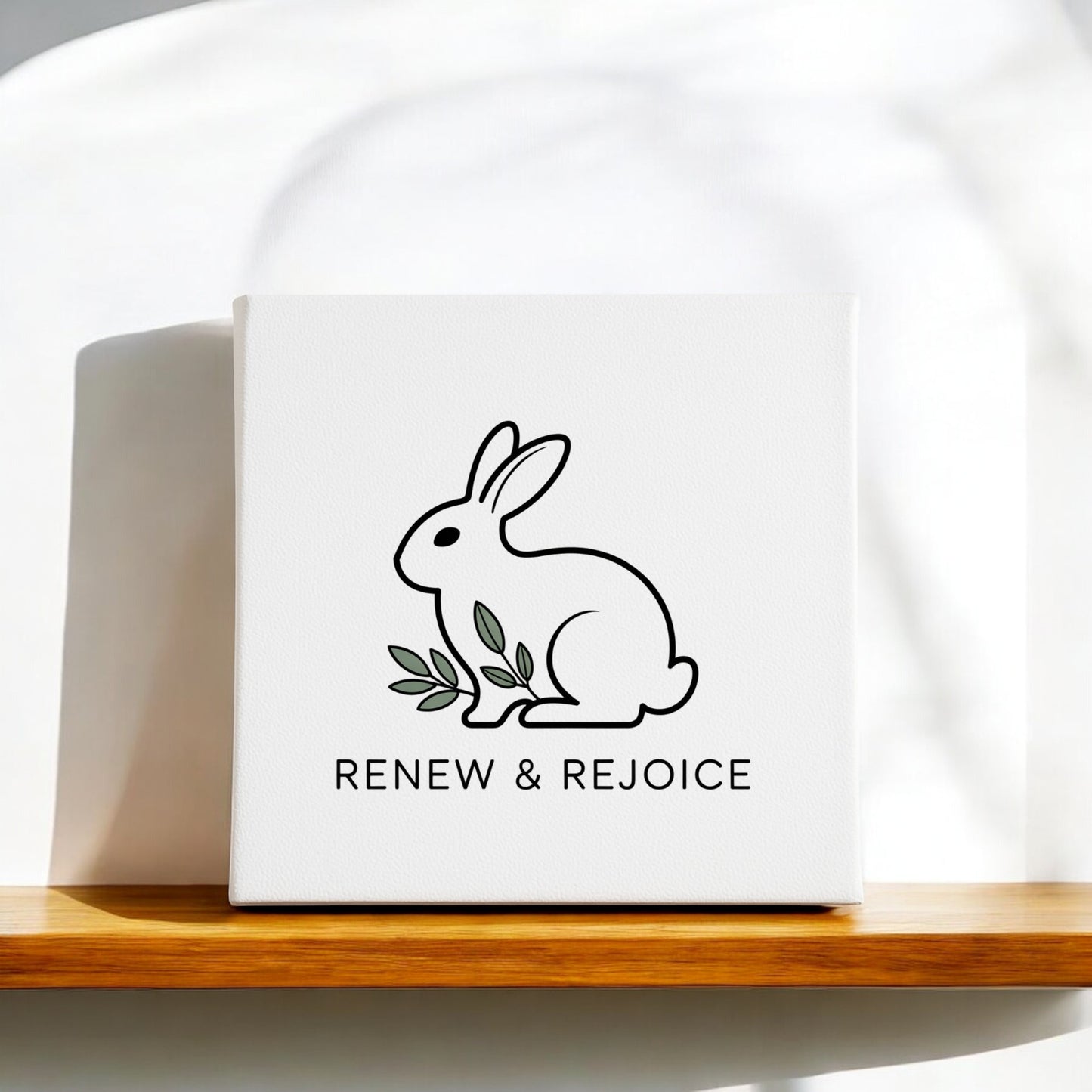 Mirabilia Boutique’s Renew & Rejoice Bunny Canvas – 8x8 Spring Wall Art features a minimalist black outline bunny with green leaves and “RENEW & REJOICE” text—perfect as Easter decor or simple spring wall art.