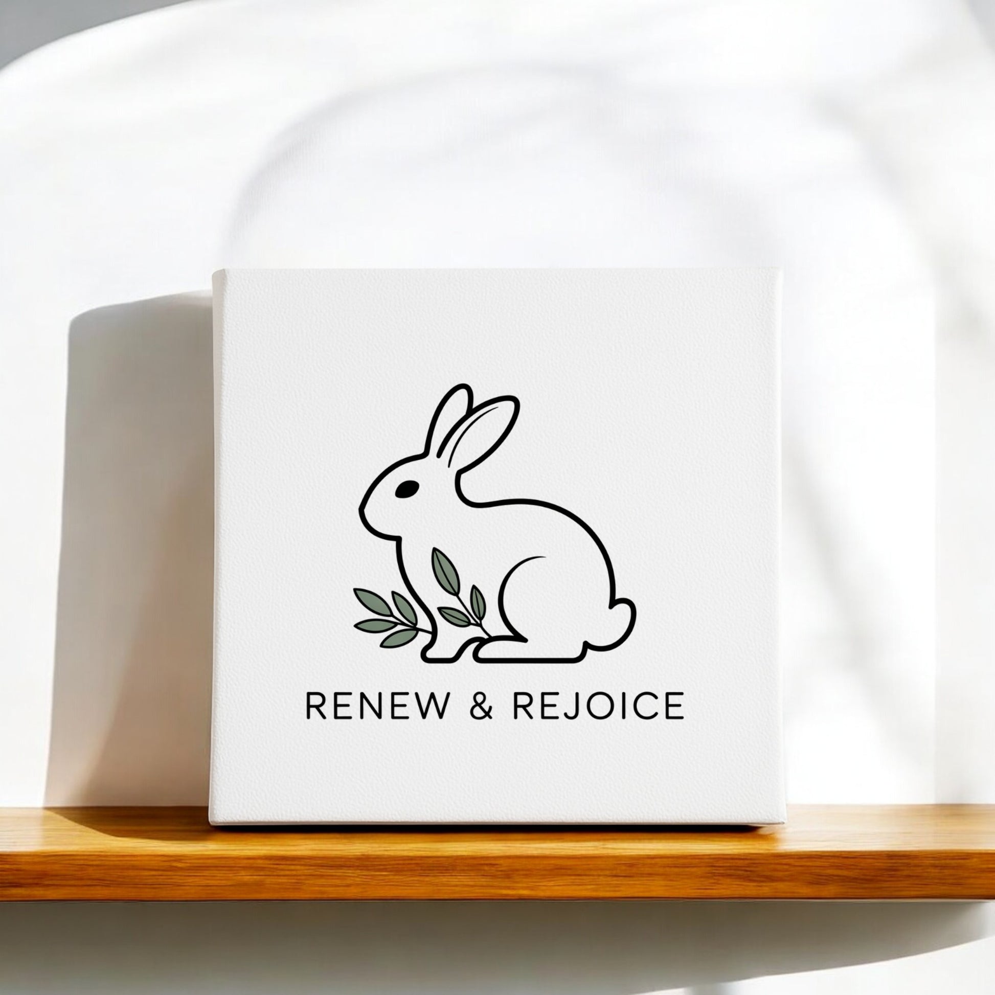 Mirabilia Boutique’s Renew & Rejoice Bunny Canvas – 8x8 Spring Wall Art features a minimalist black outline bunny with green leaves and “RENEW & REJOICE” text—perfect as Easter decor or simple spring wall art.