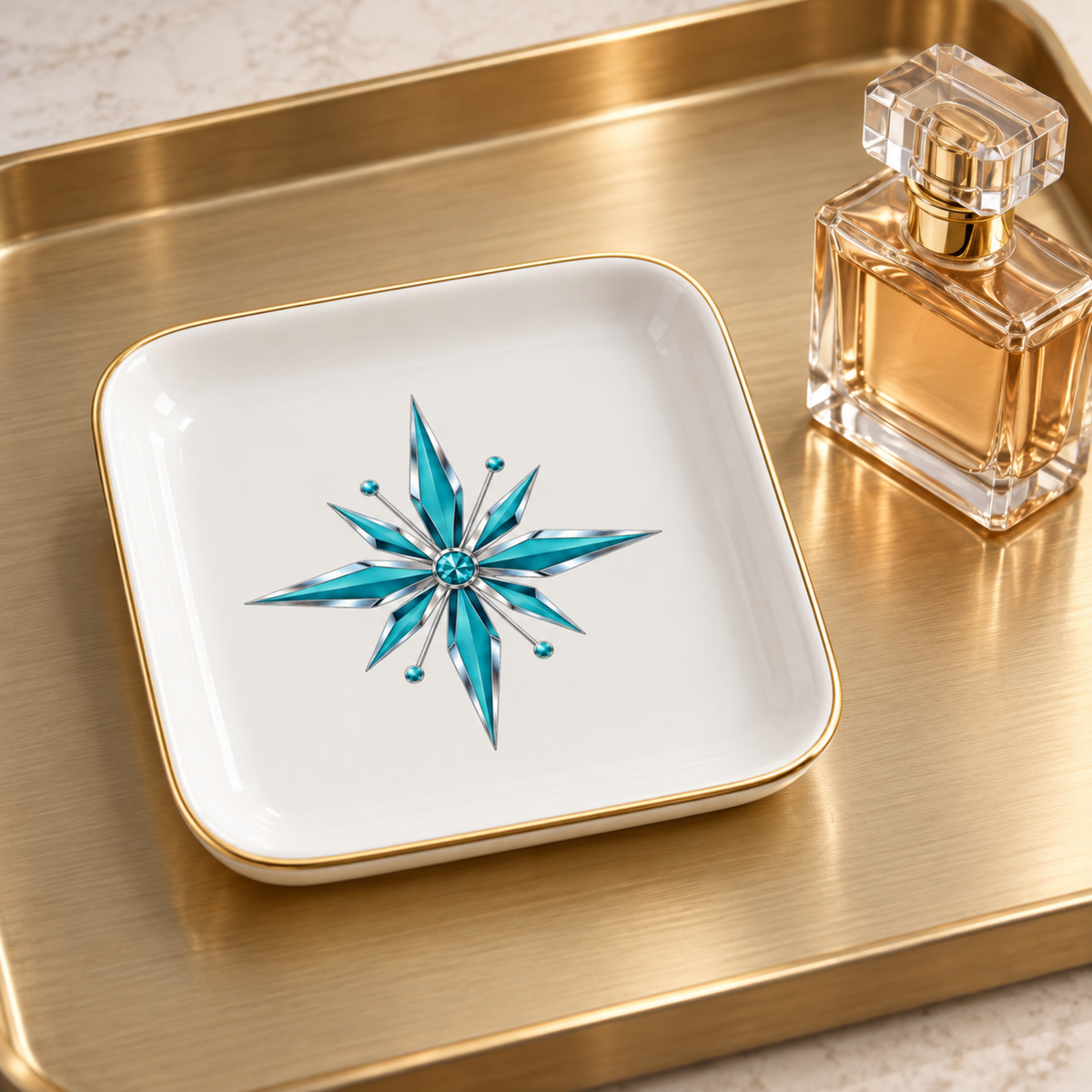 Starlite Starburst Ceramic Jewelry Tray with a gold rim and a turquoise starburst graphic, resting on a larger gold tray next to a perfume bottle.