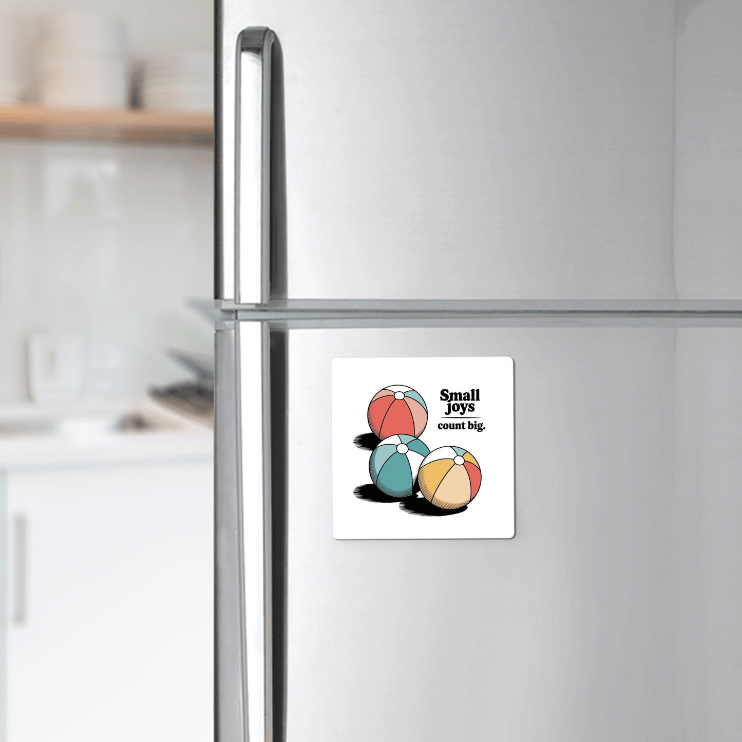 The Mirabilia Boutique Small Joys Count Big Magnet – Retro Summer Fridge Art features three colorful beach balls and uplifting text, adding cheerful summer decor to your stainless steel refrigerator. White dishes and a countertop sit in the background.