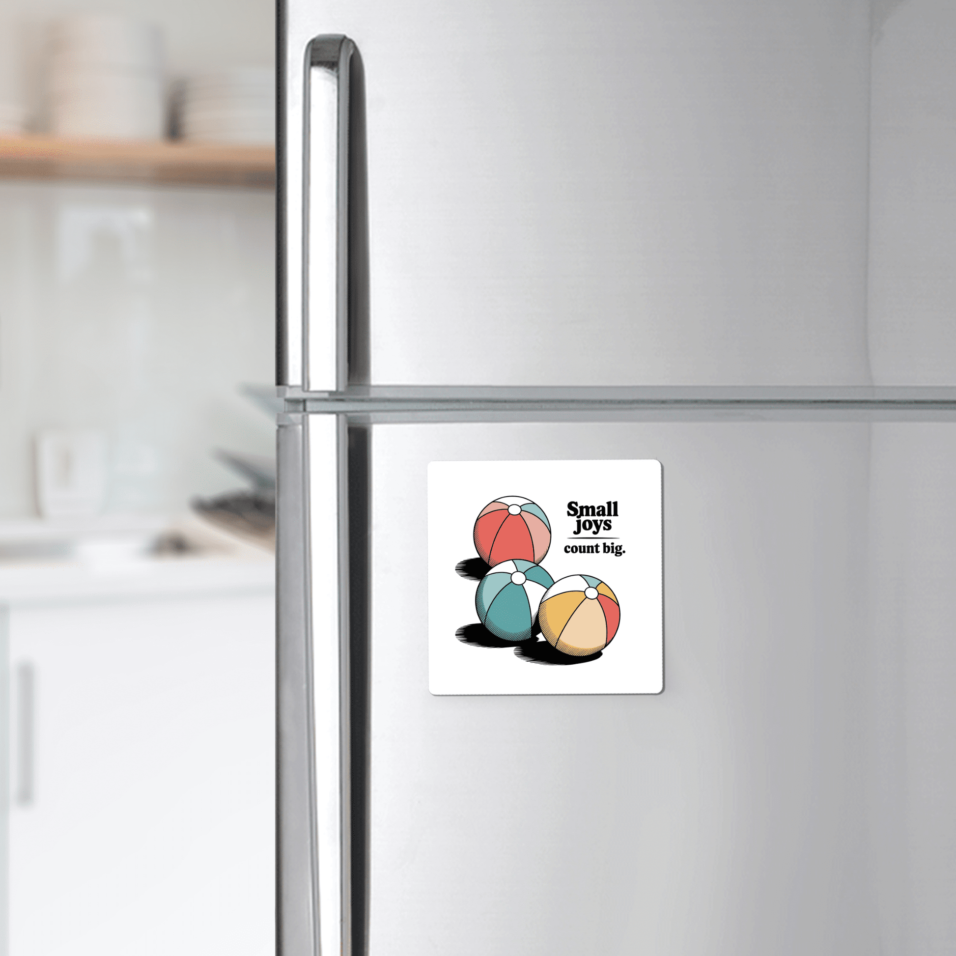 The Mirabilia Boutique Small Joys Count Big Magnet – Retro Summer Fridge Art features three colorful beach balls and uplifting text, adding cheerful summer decor to your stainless steel refrigerator. White dishes and a countertop sit in the background.