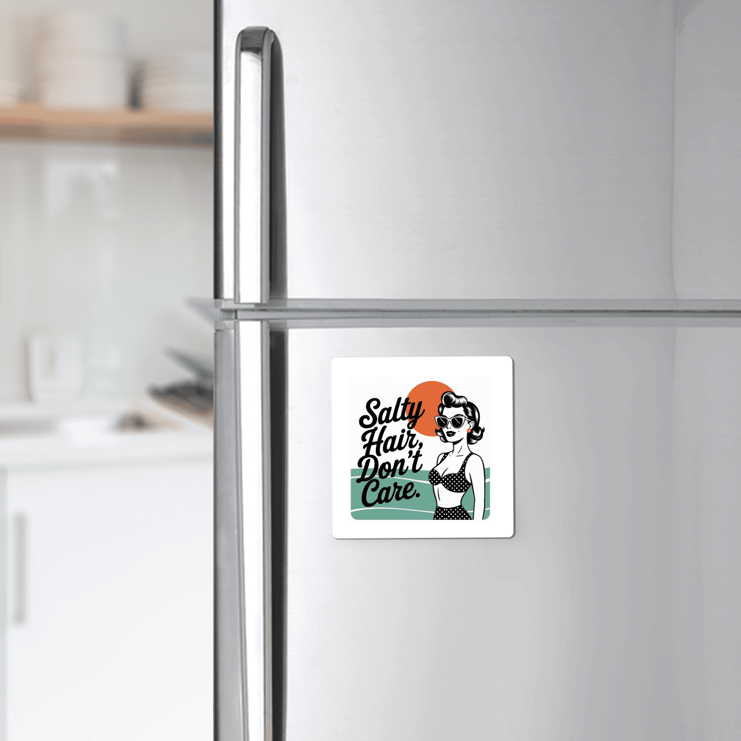 The Mirabilia Boutique "Salty Hair Don’t Care Magnet – Retro Beach Quote" features a stylish woman in sunglasses and swimsuit on an orange and teal background—fun beach house decor. The kitchen is softly blurred in the background.