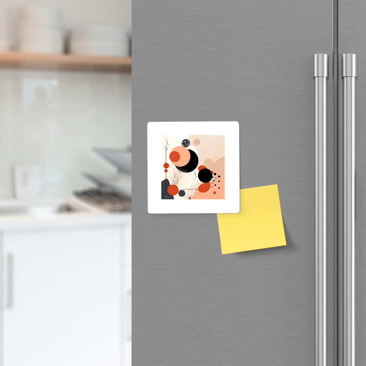 A refrigerator door features an abstract art print and a blank yellow sticky note held by the Solar Bloom Mid Century Modern Magnet from Mirabilia Boutique; modern white kitchen cabinets are seen in the background.