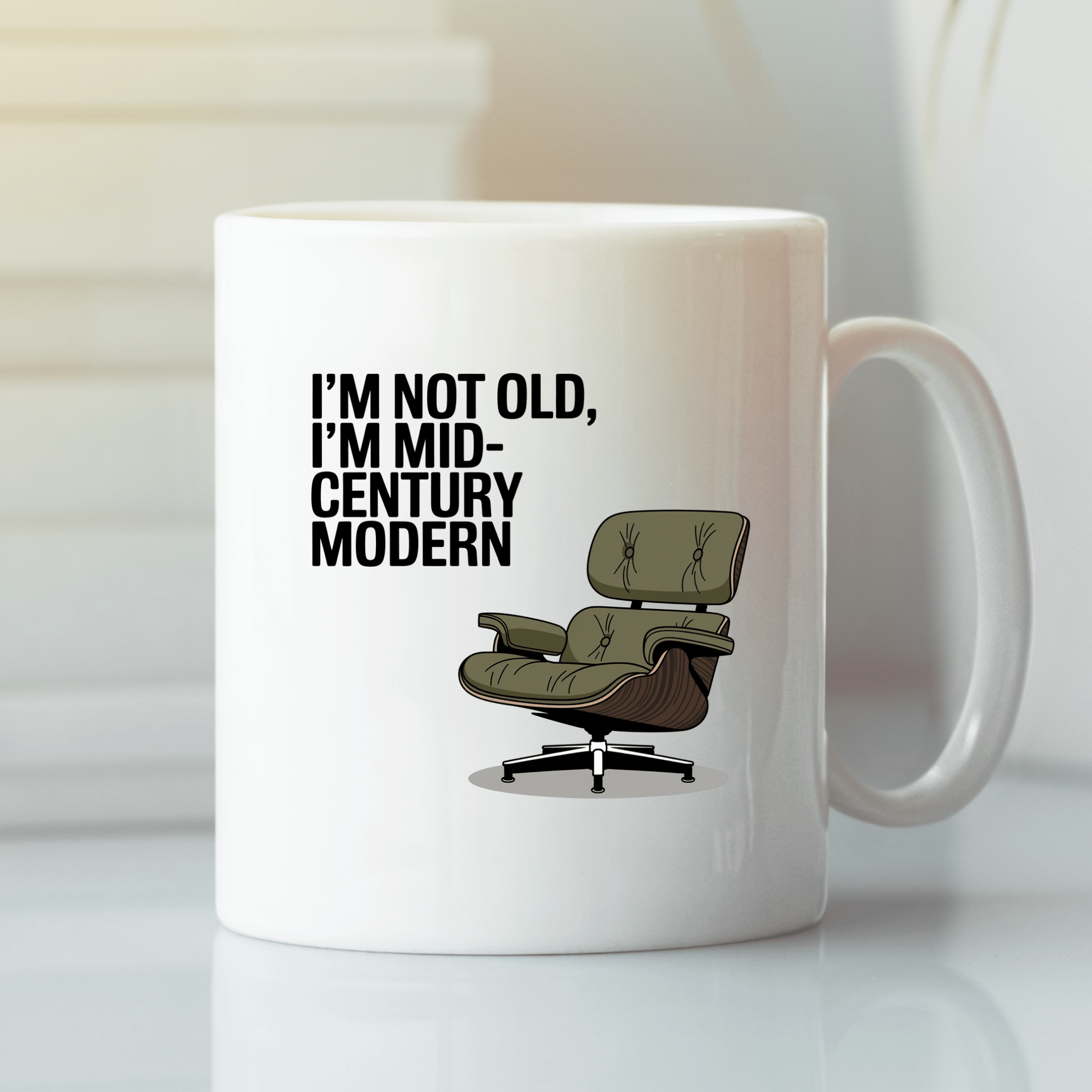 The Mid-Century Modern Mug with Retro Humor by Mirabilia Boutique features a green lounge chair and the phrase "I'M NOT OLD, I'M MID-CENTURY MODERN"—a perfect ceramic mug for vintage design lovers.