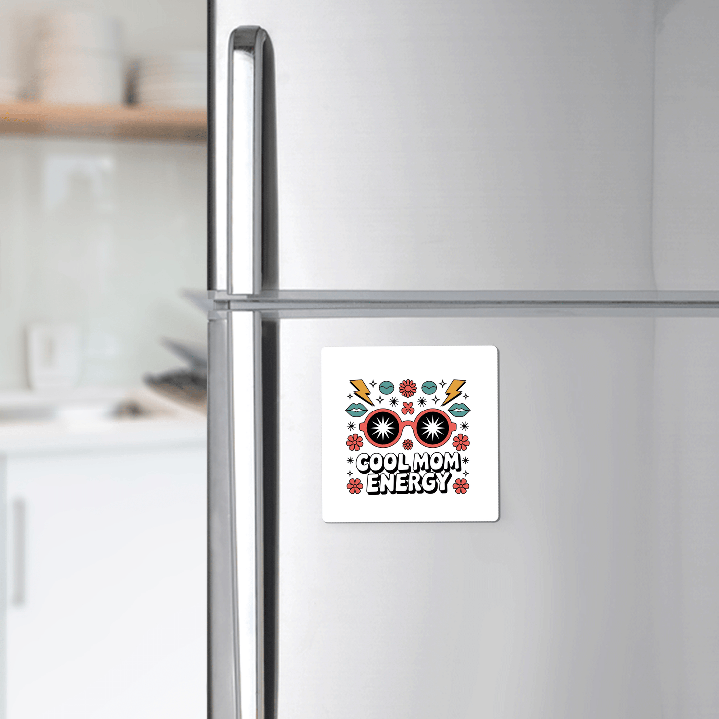 The Cool Mom Energy Magnet by Mirabilia Boutique—a bold retro Mother’s Day gift—features “COOL MOM ENERGY” with colorful flowers, hearts, and lightning bolts on a silver fridge; the softly blurred kitchen forms the backdrop.