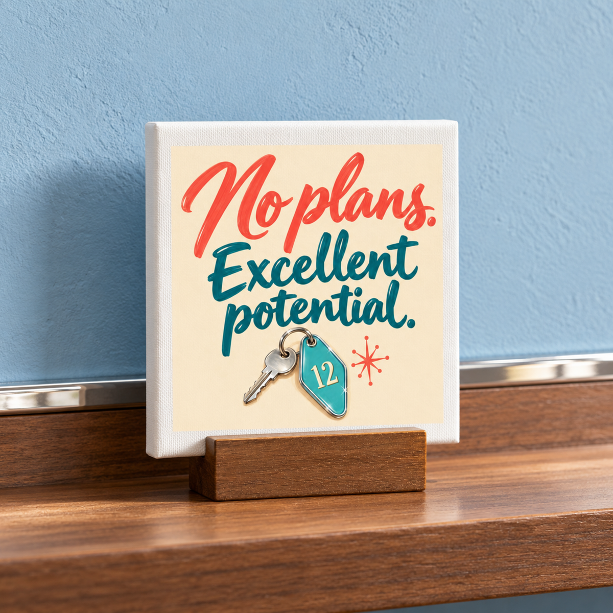 A No Plans, Excellent Potential Mini Sign | Chrome & Starlight consisting of a small square sign in a wooden stand reading “No plans. Excellent potential.” with illustrated key art of a hotel-style keychain numbered 12.