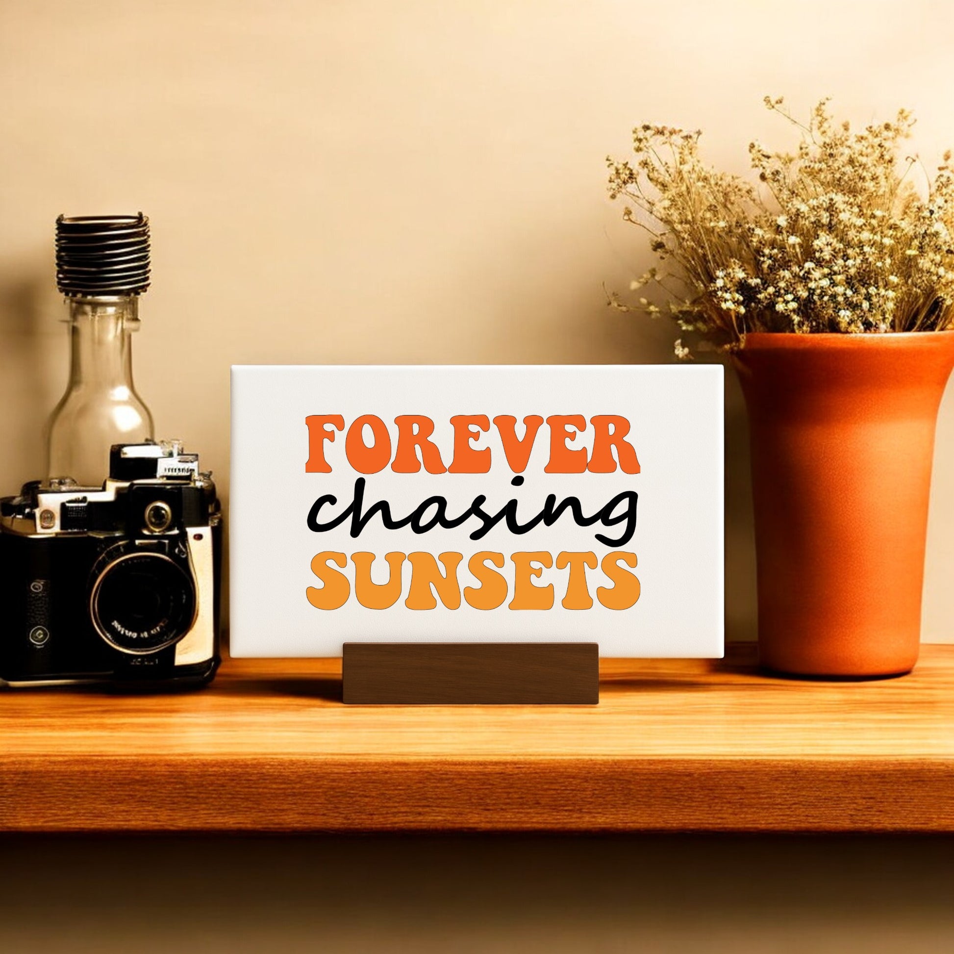 A wooden shelf displays a vintage camera, dried flowers in a terracotta vase, and the Mirabilia Boutique "Forever Chasing Sunsets Canvas – Retro Mini Sign"—the perfect decor touch for sunset chasers.