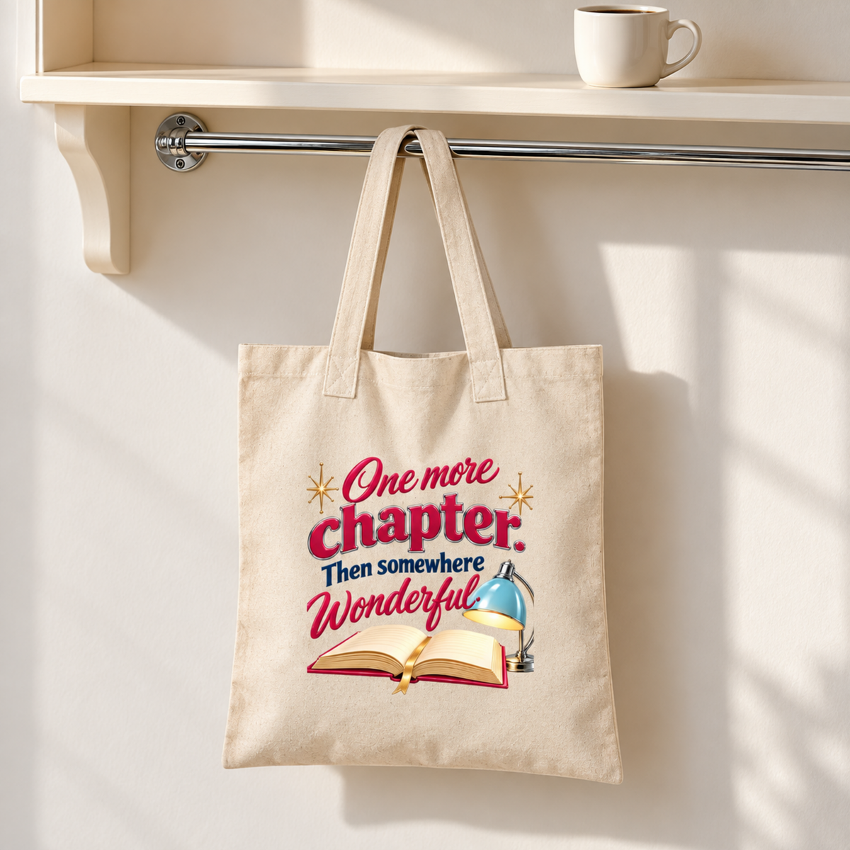 One More Chapter Book Lover Tote by Mirabilia Boutique, a canvas bag featuring an illustration of an open book, a desk lamp, and the text “One more chapter. Then somewhere Wonderful.”.