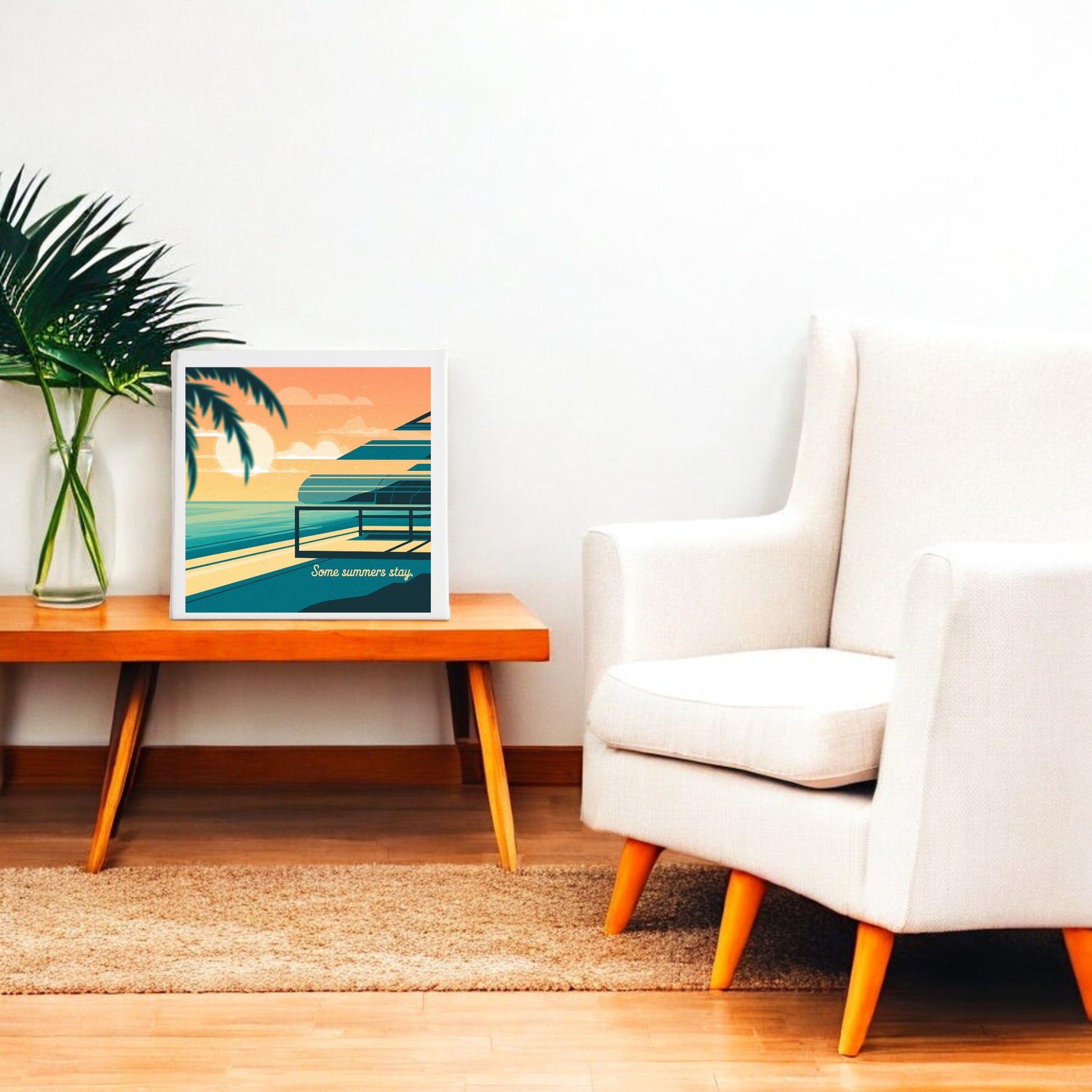 A modern, cozy living room with a white armchair, wooden table with a green plant, and Mirabilia Boutique’s Some Summers Stay Canvas—retro coastal sunset art—leaning stylishly against the wall.