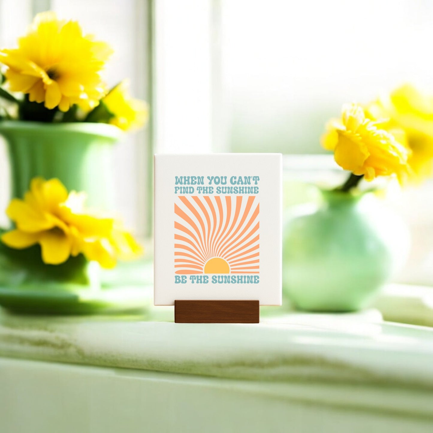 The Mirabilia Boutique "Be the Sunshine Mini Canvas – Retro Sunburst Sign" features an orange sun, a cheerful quote, and comes with a wooden stand—perfect inspirational décor with yellow flowers and soft sunlight accents.