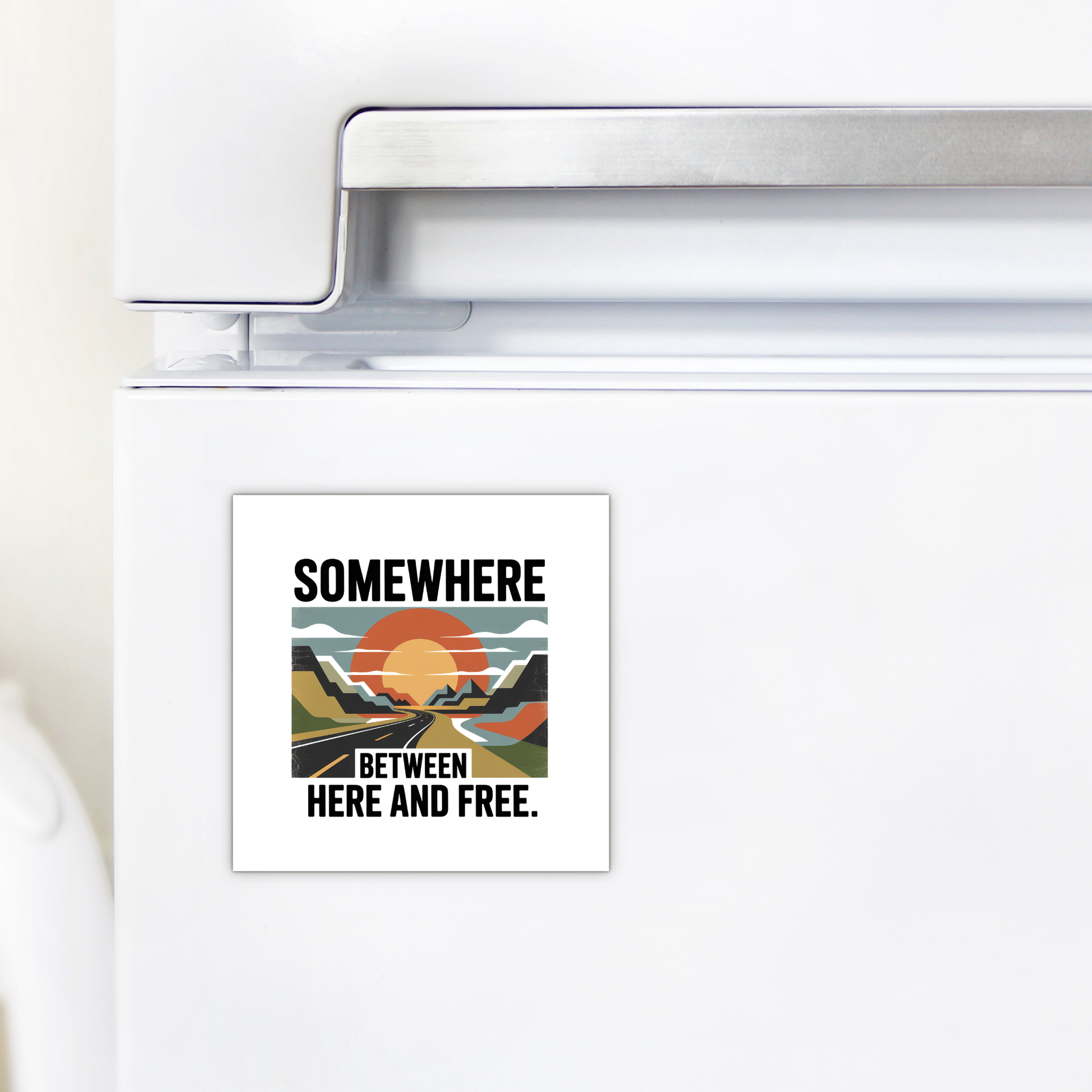 The Somewhere Between Here and Free Magnet from Mirabilia Boutique features a stylized sunset over mountains with the phrase “Somewhere between here and free,” shown here on a white refrigerator.