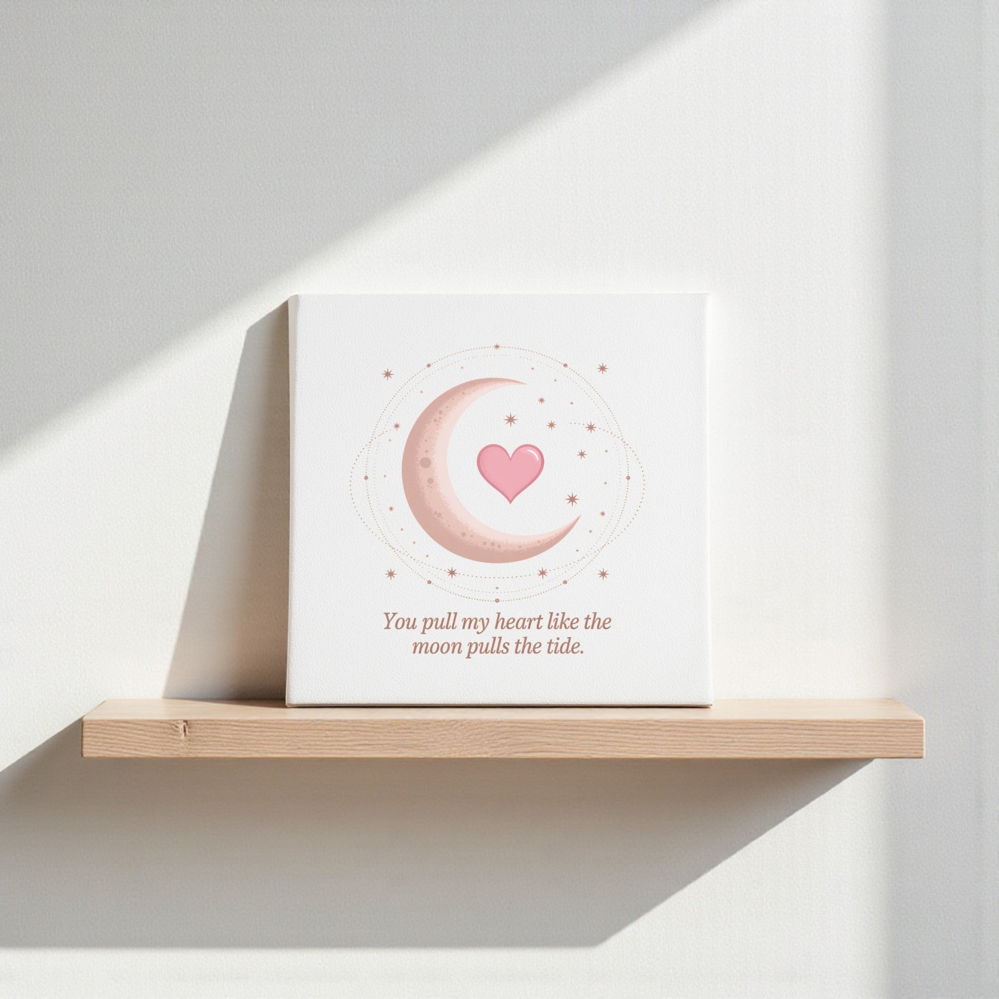 The Mirabilia Boutique "Moon Pulls the Tide Love Quote Canvas" displays pink crescent moon art with a heart and stars, plus the words, "You pull my heart like the moon pulls the tide," making dreamy celestial decor for any shelf.