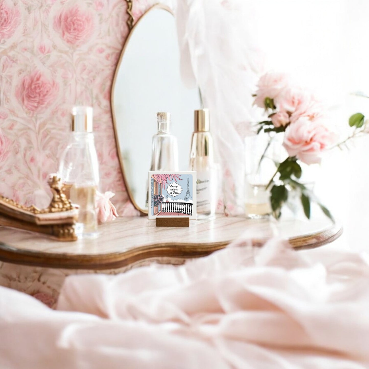 A vintage vanity with a mirror, perfume bottles, a decorative box, and pink roses is enhanced by Mirabilia Boutique's "Spring Whispers in Paris Mini Sign – Soft Paris Spring," creating an elegant, romantic spring décor ambiance.