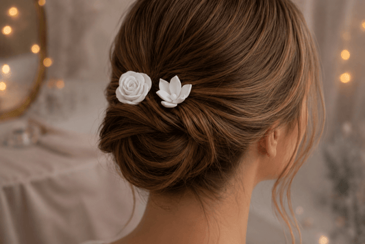 A woman with brown hair styled in a low updo wears the Mirabilia Boutique Rose & Lotus Hair Fork Bundle in Matte Cotton White, floral accessories shaped like a rose and lotus. Soft, warm fairy lights glow in the blurred background.