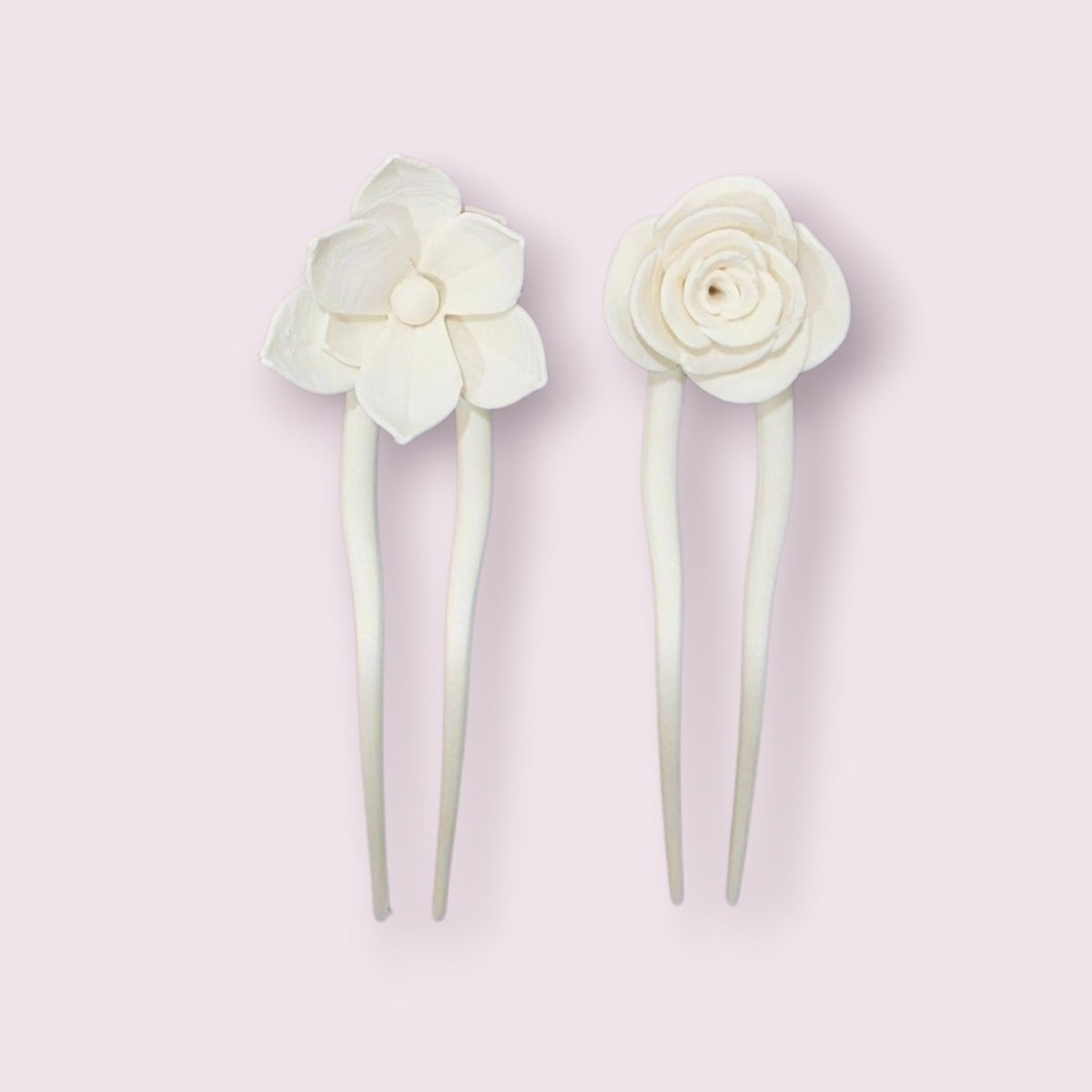 The Rose & Lotus Hair Fork Bundle in Matte Cotton White by Mirabilia Boutique features two-prong hair forks—one with a five-petal lotus, the other a rose—making elegant floral accessories. Displayed on a pale pink background.