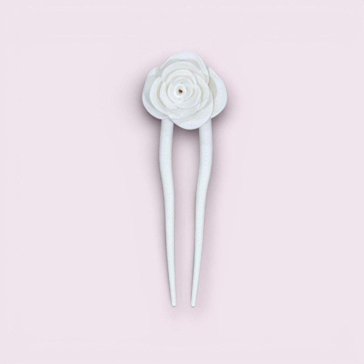 The Mirabilia Boutique Rose Hair Fork in Matte Cotton White features two prongs and a decorative white rose, elegantly displayed against a light pink background.