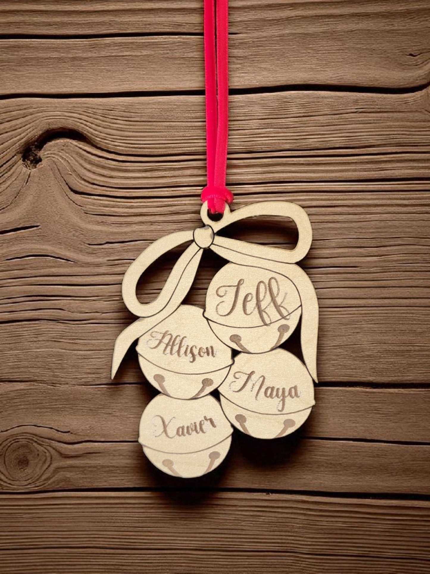 The Mirabilia Boutique Custom Family Christmas Ornament is a laser-cut wooden tree decoration featuring four personalized jingle bells with engraved names, tied with a bow and hanging from a red ribbon.