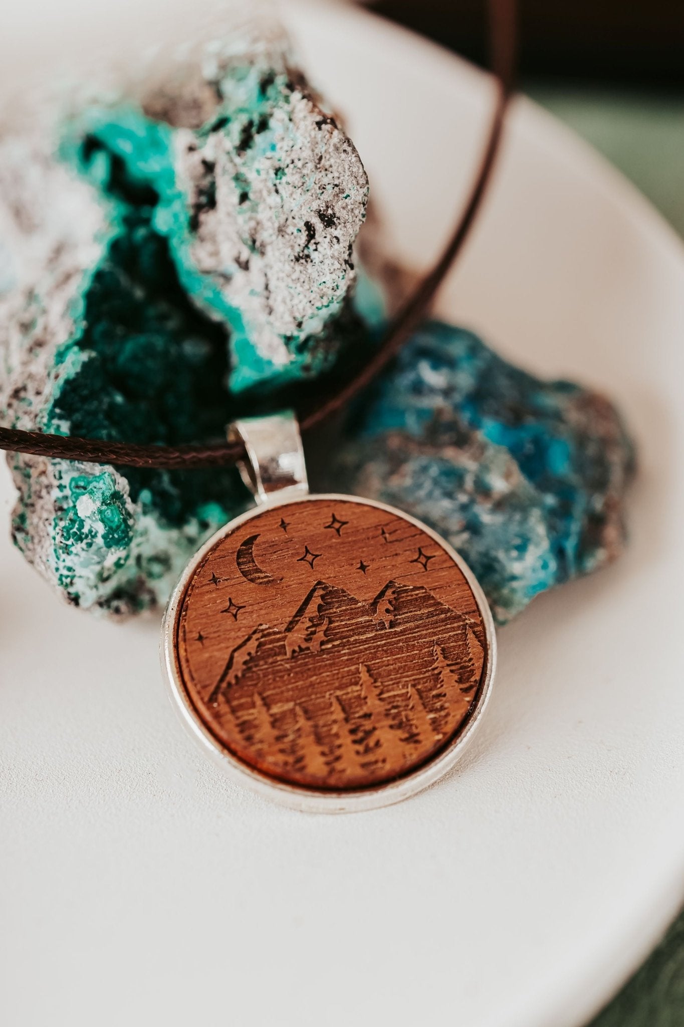 The Engraved Wood Pendant Necklace – Mountain Night Sky Design by Mirabilia Boutique showcases mountains, trees, a crescent moon, and stars in natural wood, perfect for nature lovers.