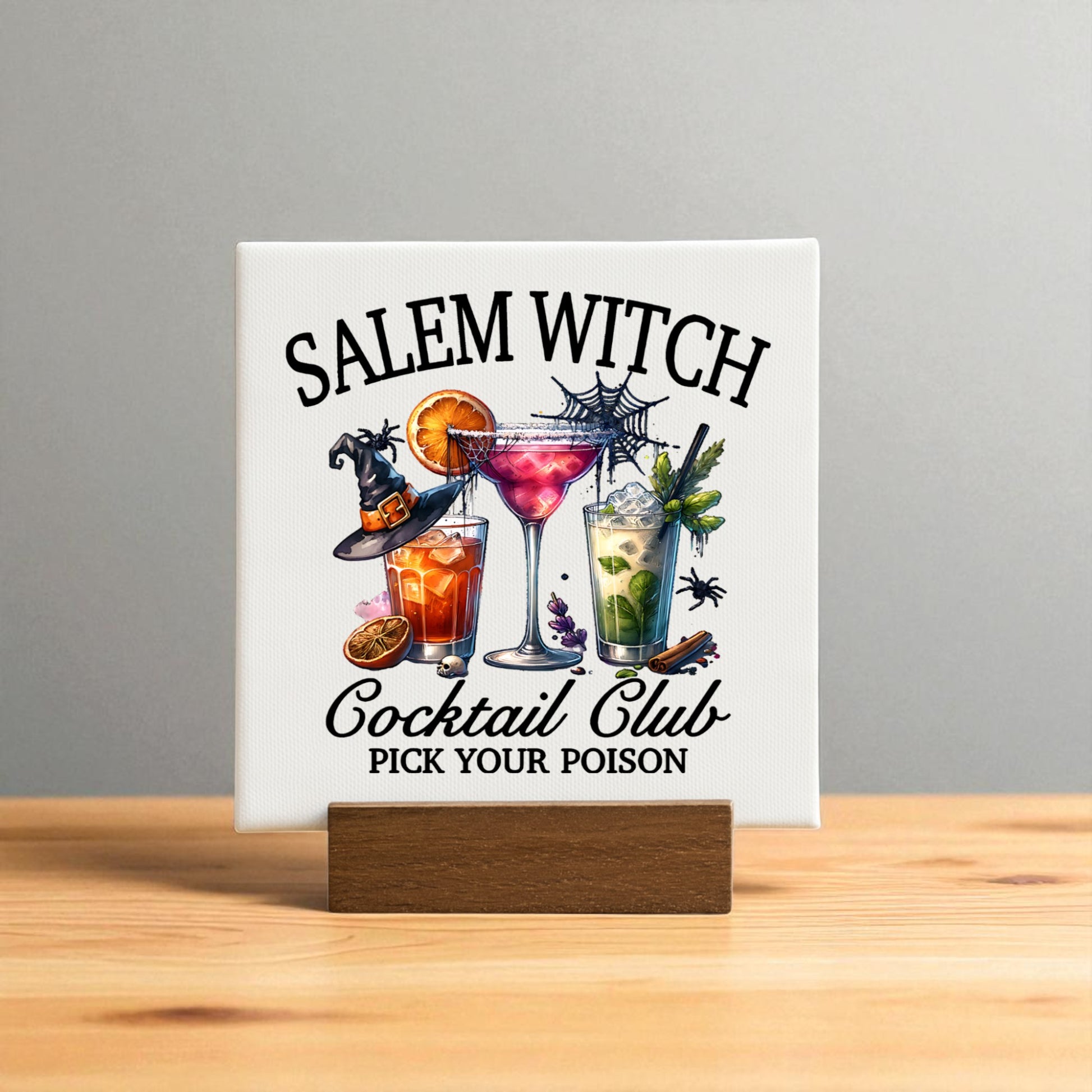 The Salem Witch Cocktail Club Mini Sign by Mirabilia Boutique is a square Halloween bar decor piece on a wooden stand, featuring three colorful spooky cocktails and the phrase "Pick Your Poison" on a light gray background.