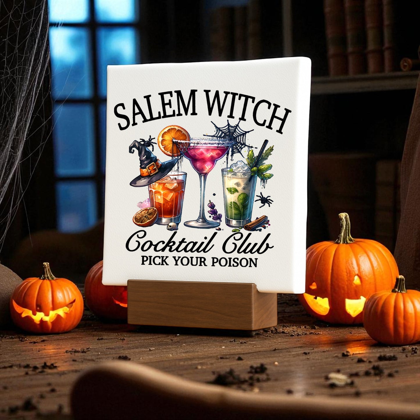 Create a spooky vibe with the Salem Witch Cocktail Club Mini Sign by Mirabilia Boutique—Halloween bar decor featuring eerie cocktail art, perfect among glowing jack-o'-lanterns and festive decorations in a dimly lit room.