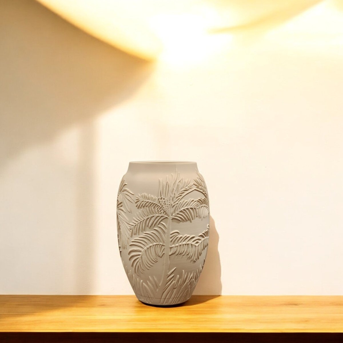 The Sand Palm Desert Vase for Summer Decor by Mirabilia Boutique, featuring a palm tree motif in matte sand beige, rests on wood against an off-white wall—beautifully lit and perfect for adding desert-inspired charm to your space.