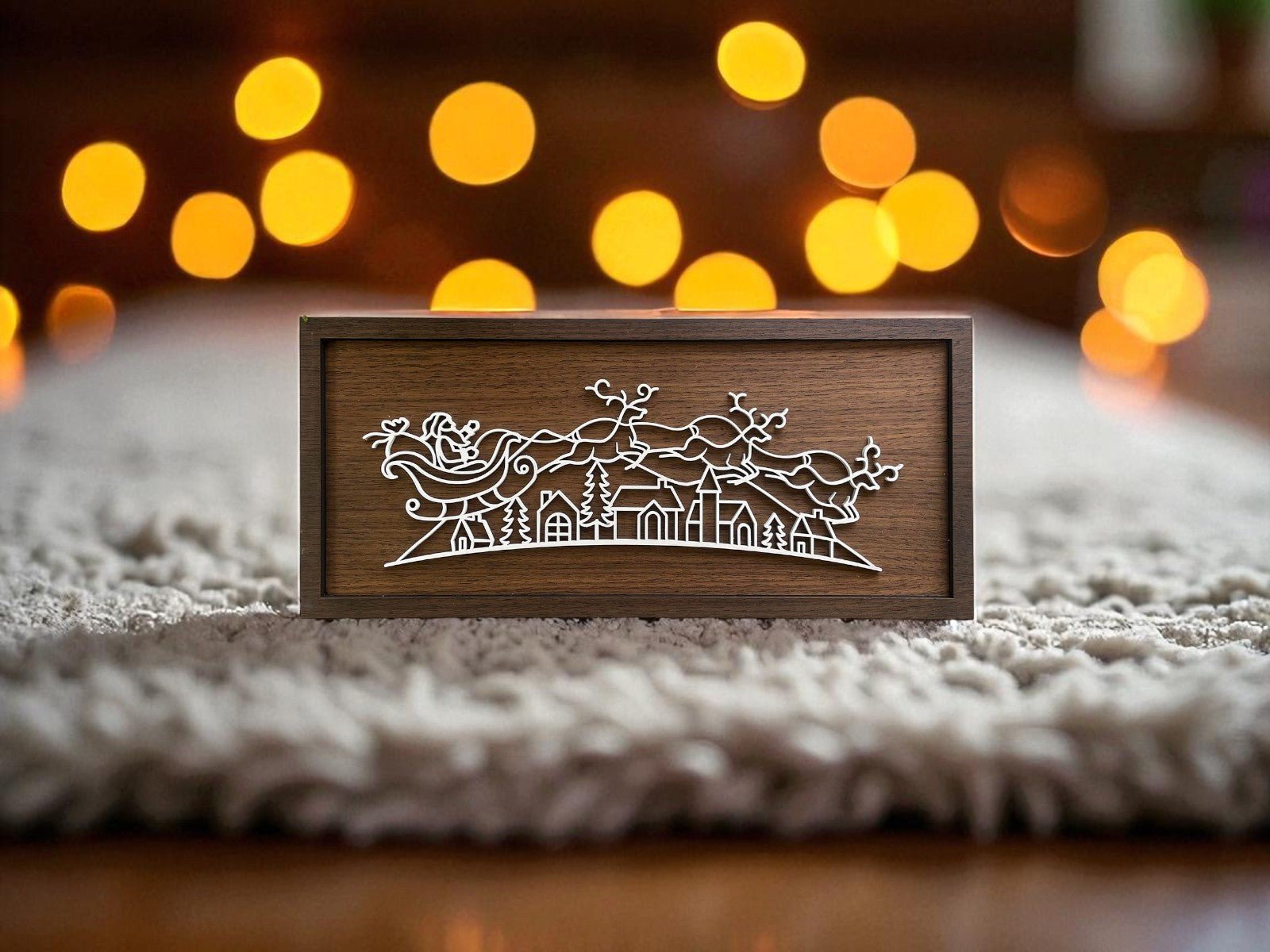 The Santa Sleigh Laser Cut Sign by Mirabilia Boutique is a modern Christmas wall art featuring a white outline of Santa in his sleigh with reindeer flying over a village—perfect for minimalist holiday decor.