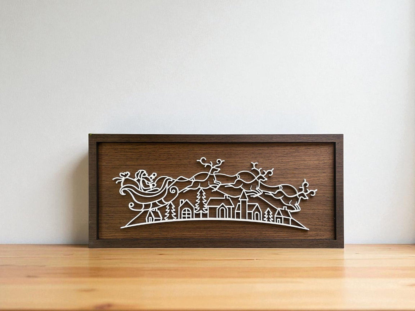 The Santa Sleigh Laser Cut Sign by Mirabilia Boutique features a modern wooden frame with Santa’s sleigh and reindeer over a village, making it perfect minimalist Christmas wall art for your home decor.