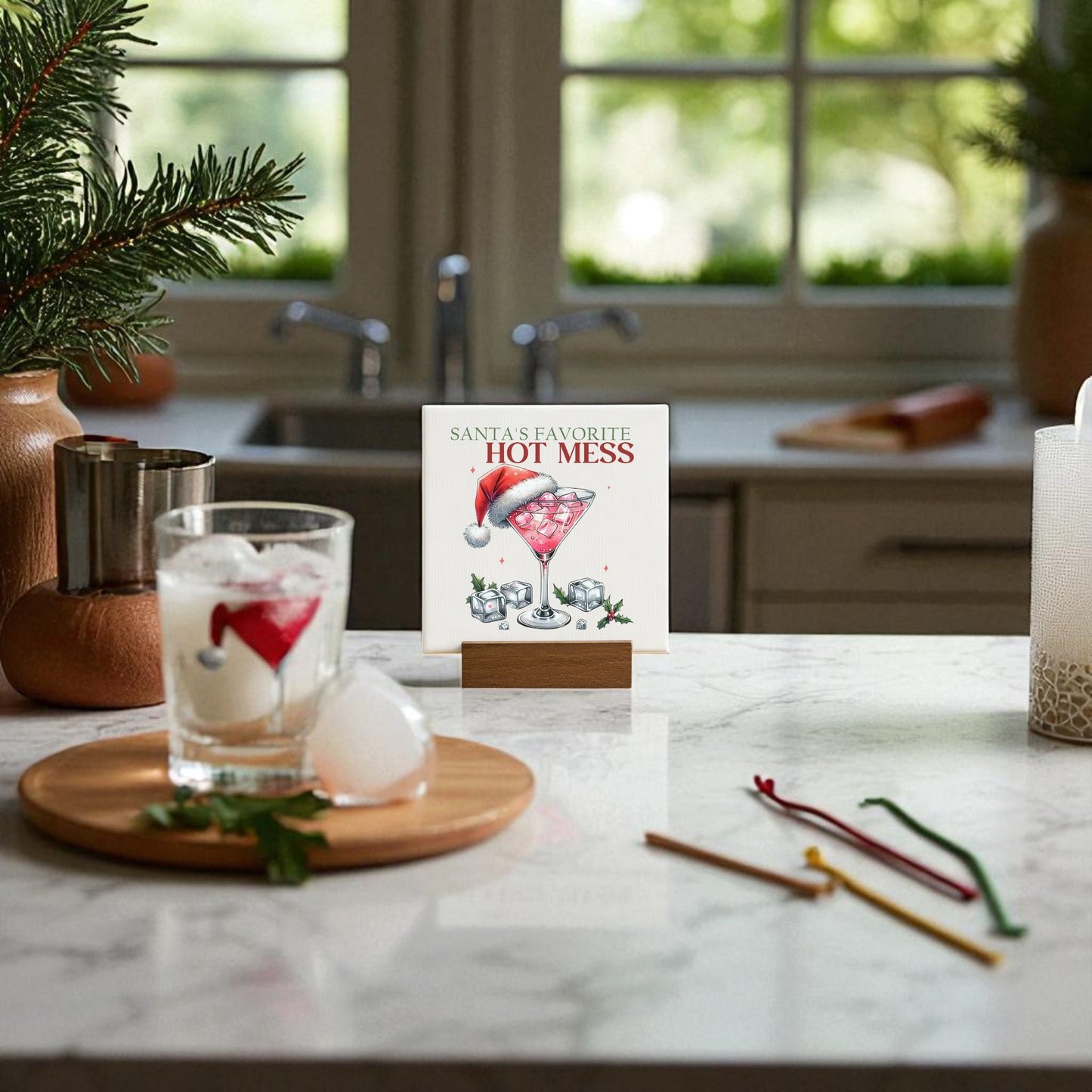 A kitchen counter features Mirabilia Boutique’s "Santa’s Favorite Hot Mess Mini Sign," a Santa hat, festive drink stirrers, and holiday greenery—perfect Christmas bar decor and a fun hostess gift.
