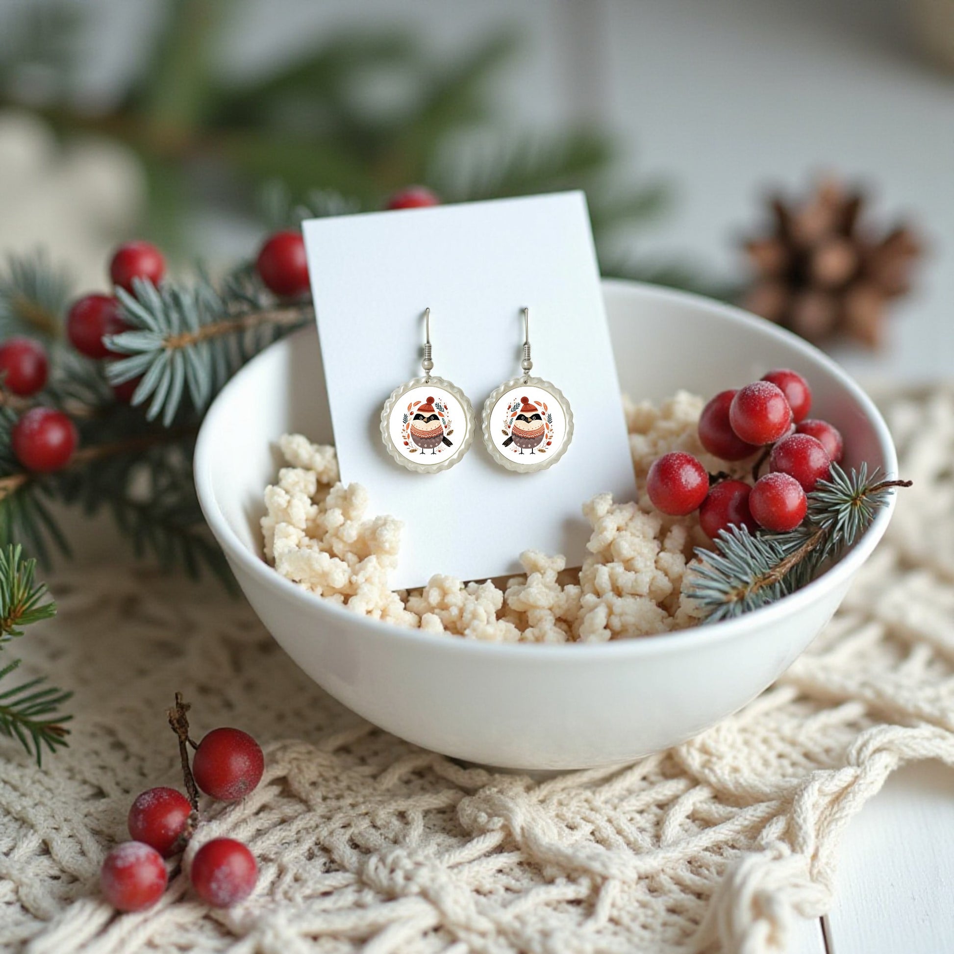 A white bowl of rice holds a card with Mirabilia Boutique’s Scandi Christmas Bird Earrings—festive, hypoallergenic jewelry. Surrounded by pine, berries, and a pinecone, the display captures cozy Scandinavian winter style.