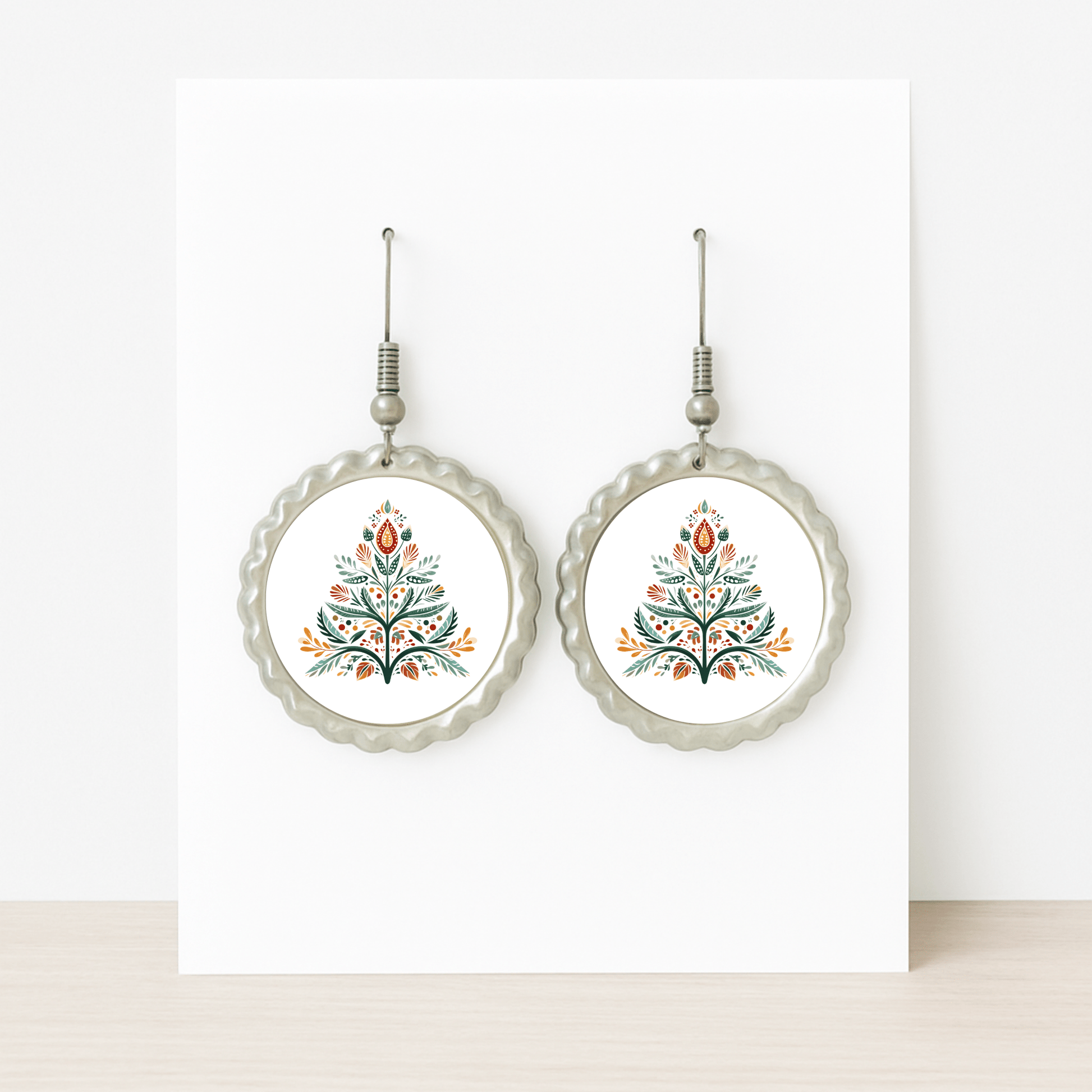Scandi Christmas Tree Earrings by Mirabilia Boutique: round Nordic-inspired design with scalloped silver edges and a vibrant red, green, yellow, and black floral folk art motif on white.