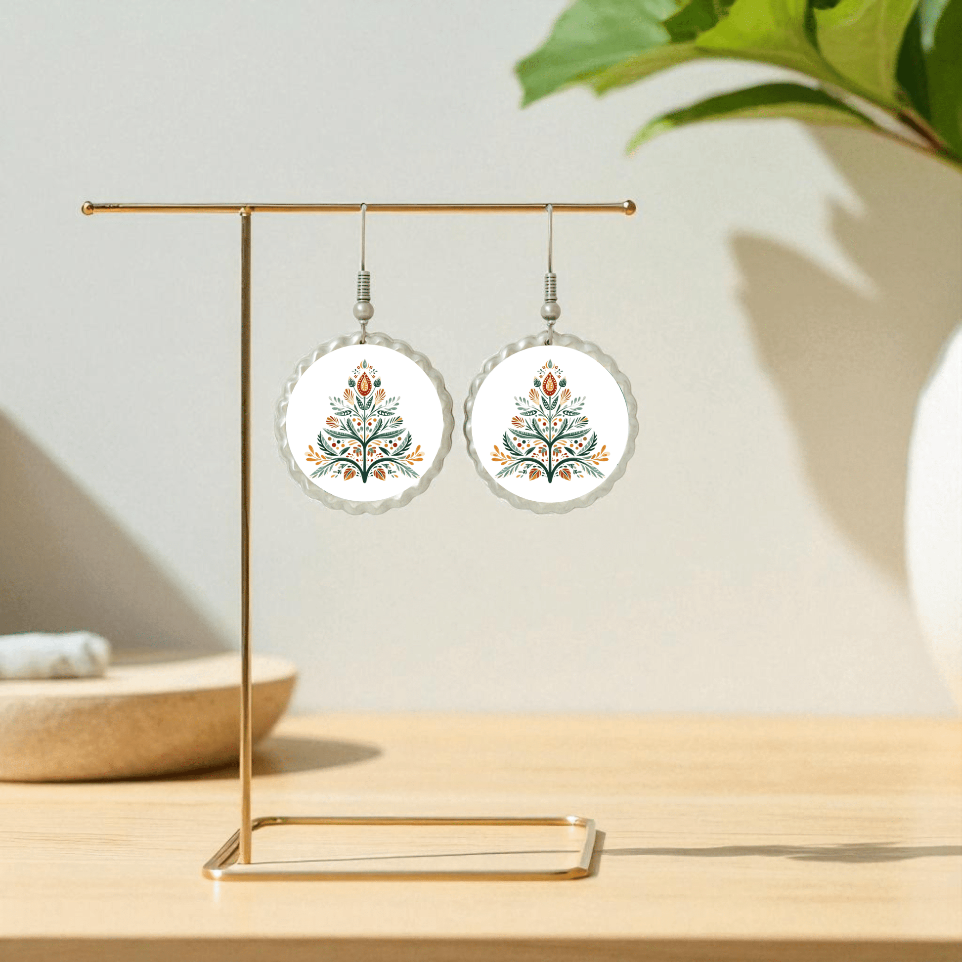 The Scandi Christmas Tree Earrings by Mirabilia Boutique feature Nordic-inspired floral designs in orange, green, and blue. Displayed on a gold stand with a festive touch, they make perfect minimalist holiday jewelry for any occasion.
