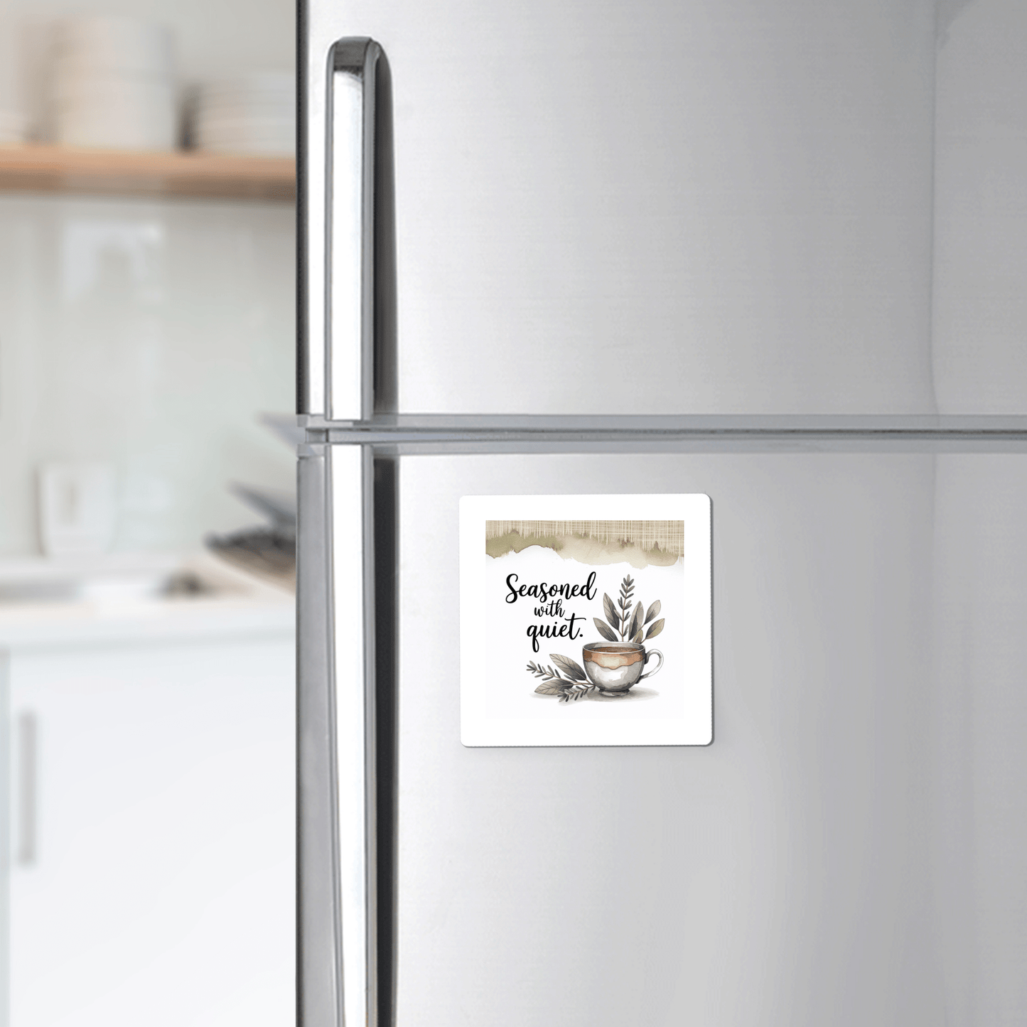 The Seasoned with Quiet Magnet by Mirabilia Boutique rests on a stainless steel fridge, featuring a watercolor teacup and green herbs—an ideal calm kitchen decor gift for mindfulness lovers.