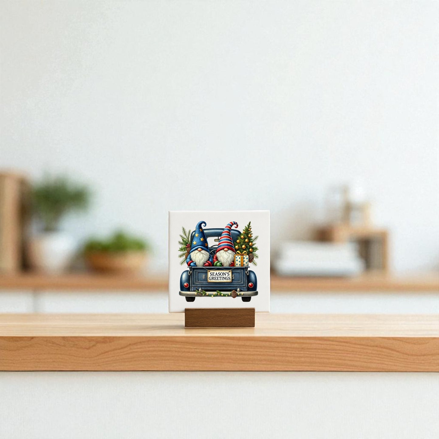 The Mirabilia Boutique Season’s Greetings Gnome Mini Sign, a 4x4 holiday canvas featuring a festive gnome scene and “Merry Christmas” message, sits on a wooden stand atop a light surface with a softly blurred background.