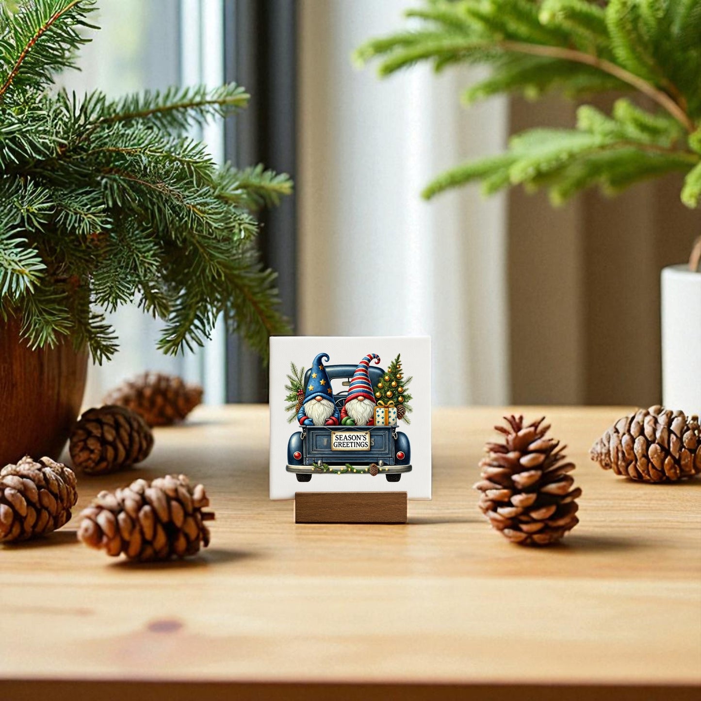 The Mirabilia Boutique Season’s Greetings Gnome Mini Sign, a 4x4 holiday canvas on a wooden stand, sits among pinecones and branches. Its festive gnome design brings cheerful holiday charm to your decor as sunlight streams through the window.