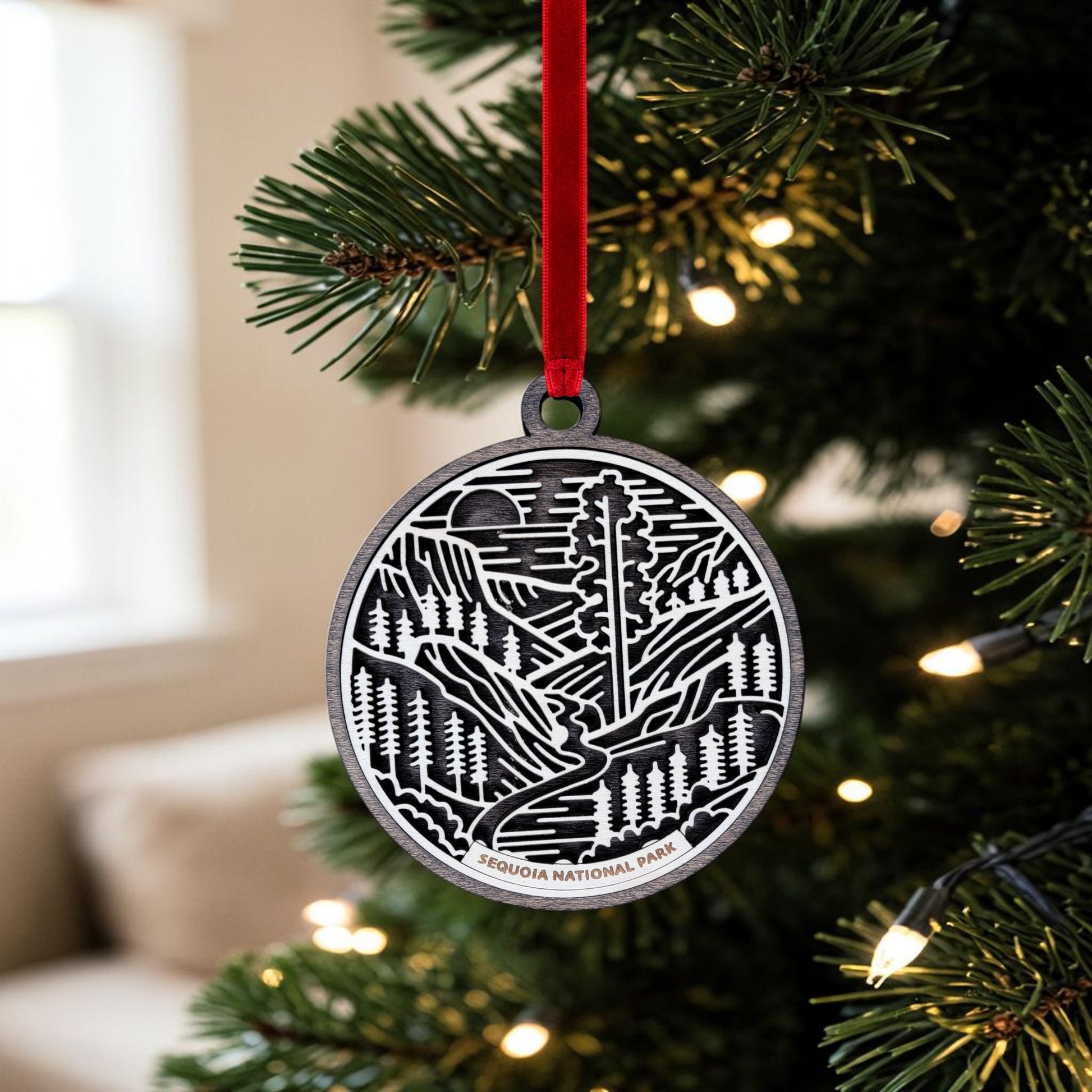 Handcrafted by Mirabilia Boutique, the Sequoia National Park Line Art Christmas Ornament showcases a detailed tree design and hangs from a red ribbon on a glowing Christmas tree.