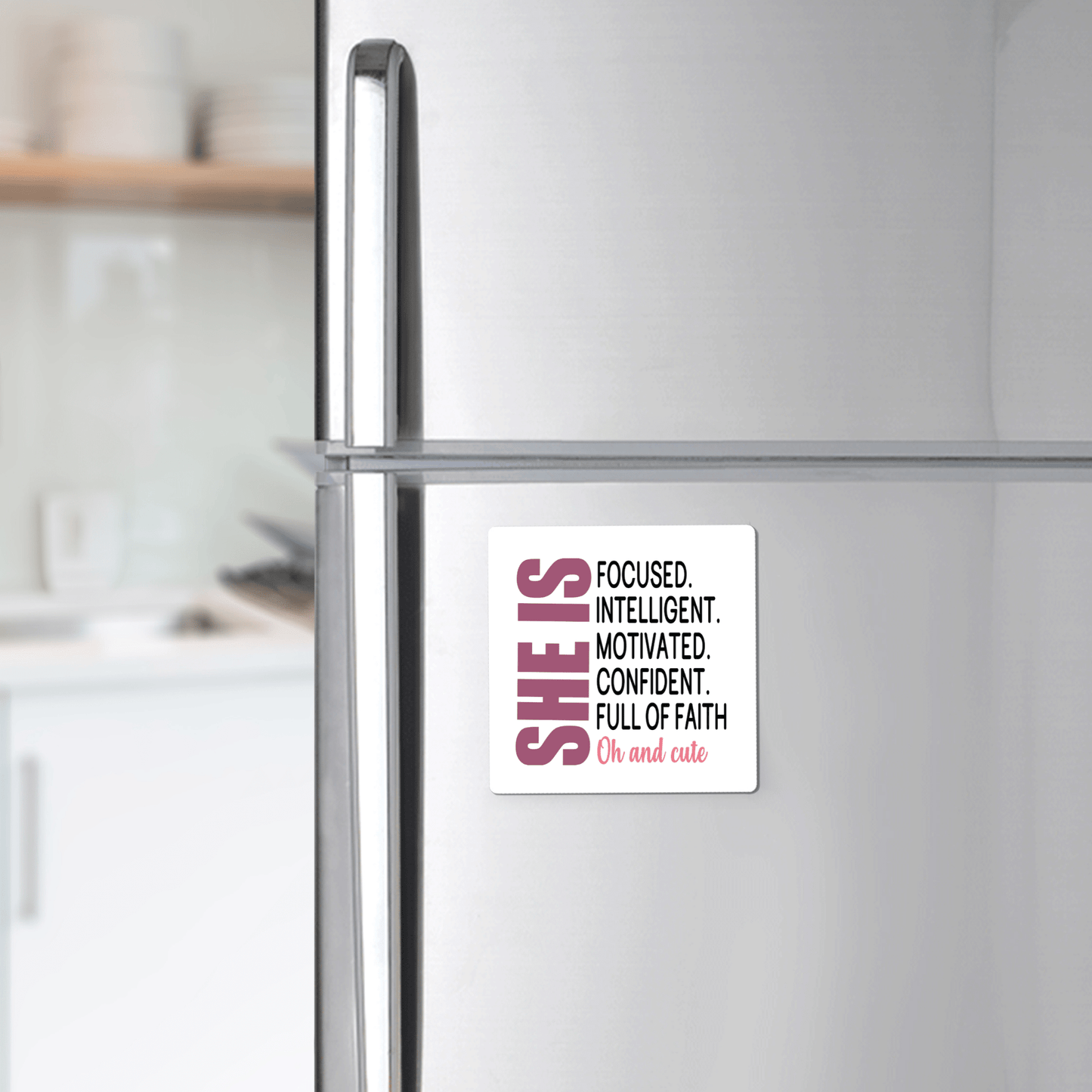 A stainless steel fridge displays the Mirabilia Boutique "She Is Motivated & Confident" magnet, featuring the quote: "SHE IS FOCUSED. INTELLIGENT. MOTIVATED. CONFIDENT. FULL OF FAITH. Oh and cute." An uplifting inspirational gift for her.