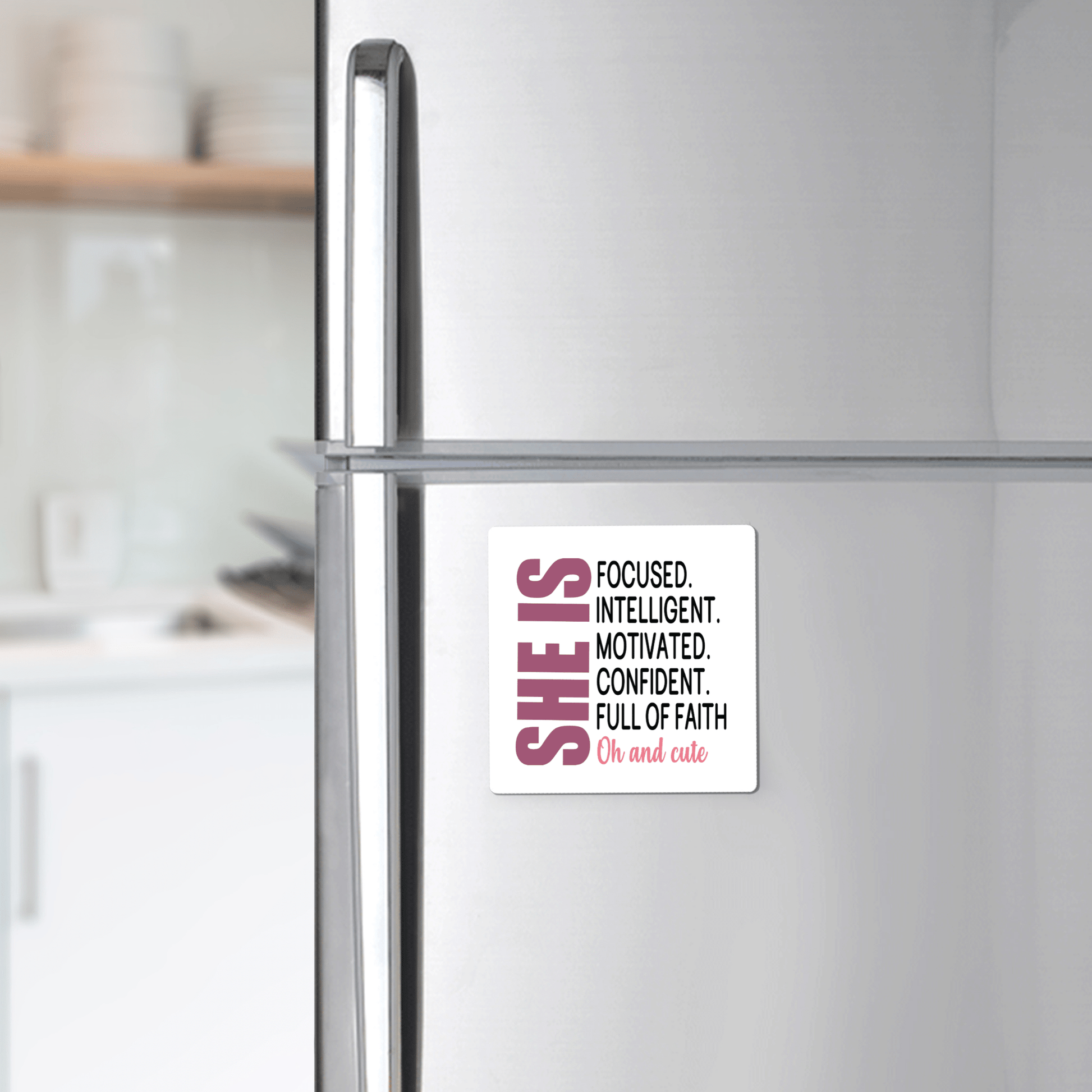 A stainless steel fridge displays the Mirabilia Boutique "She Is Motivated & Confident" magnet, featuring the quote: "SHE IS FOCUSED. INTELLIGENT. MOTIVATED. CONFIDENT. FULL OF FAITH. Oh and cute." An uplifting inspirational gift for her.
