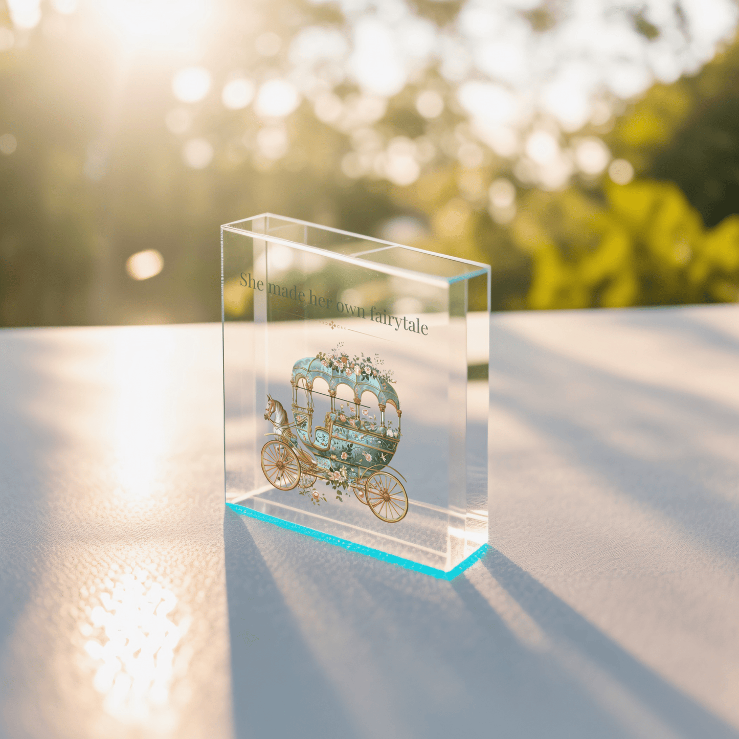 The She Made Her Own Fairytale Acrylic Quote Block by Mirabilia Boutique features an illustrated carriage and inspiring words, resting on a sunlit surface—an ideal empowerment gift available in 3x3 or 4x4 sizes.
