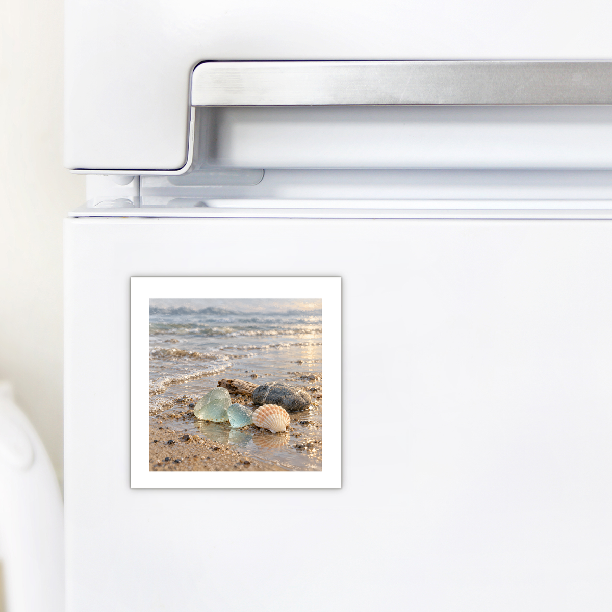 Sea Glass Morning Magnet on a white refrigerator featuring a coastal illustration of sea glass, a seashell, and a stone on a wet sandy beach.