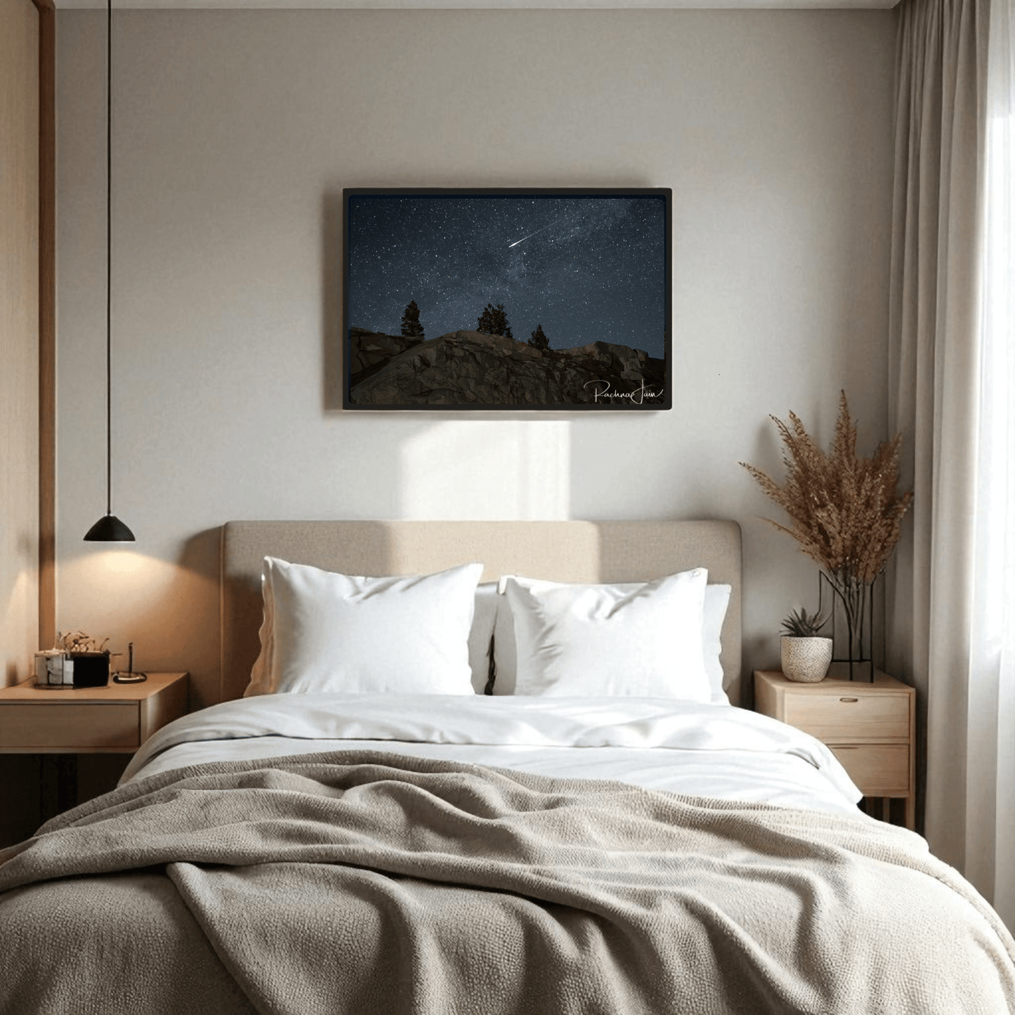 A cozy bedroom features a beige bed with white pillows and Mirabilia Boutique's "Shooting Star at Olmsted Point" night sky art above the headboard. Wooden nightstands display a pendant light and dried plants, while sheer curtains let in soft light.