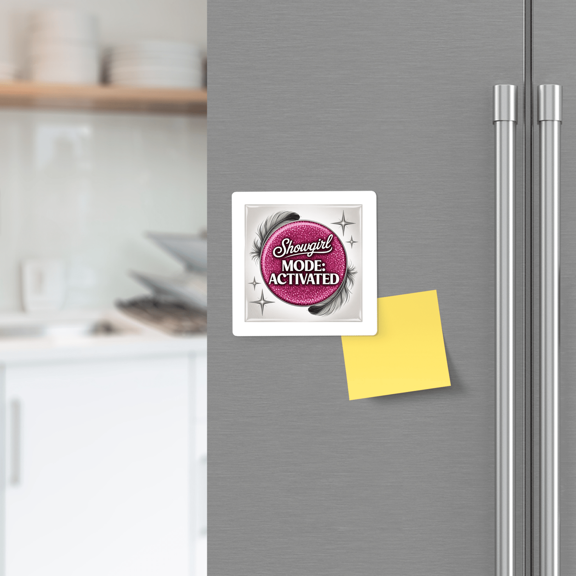 A Mirabilia Boutique “Showgirl Mode Activated” Magnet in glam pink decorates a fridge door beside a blank yellow sticky note; kitchen shelves and counter are softly blurred in the background.