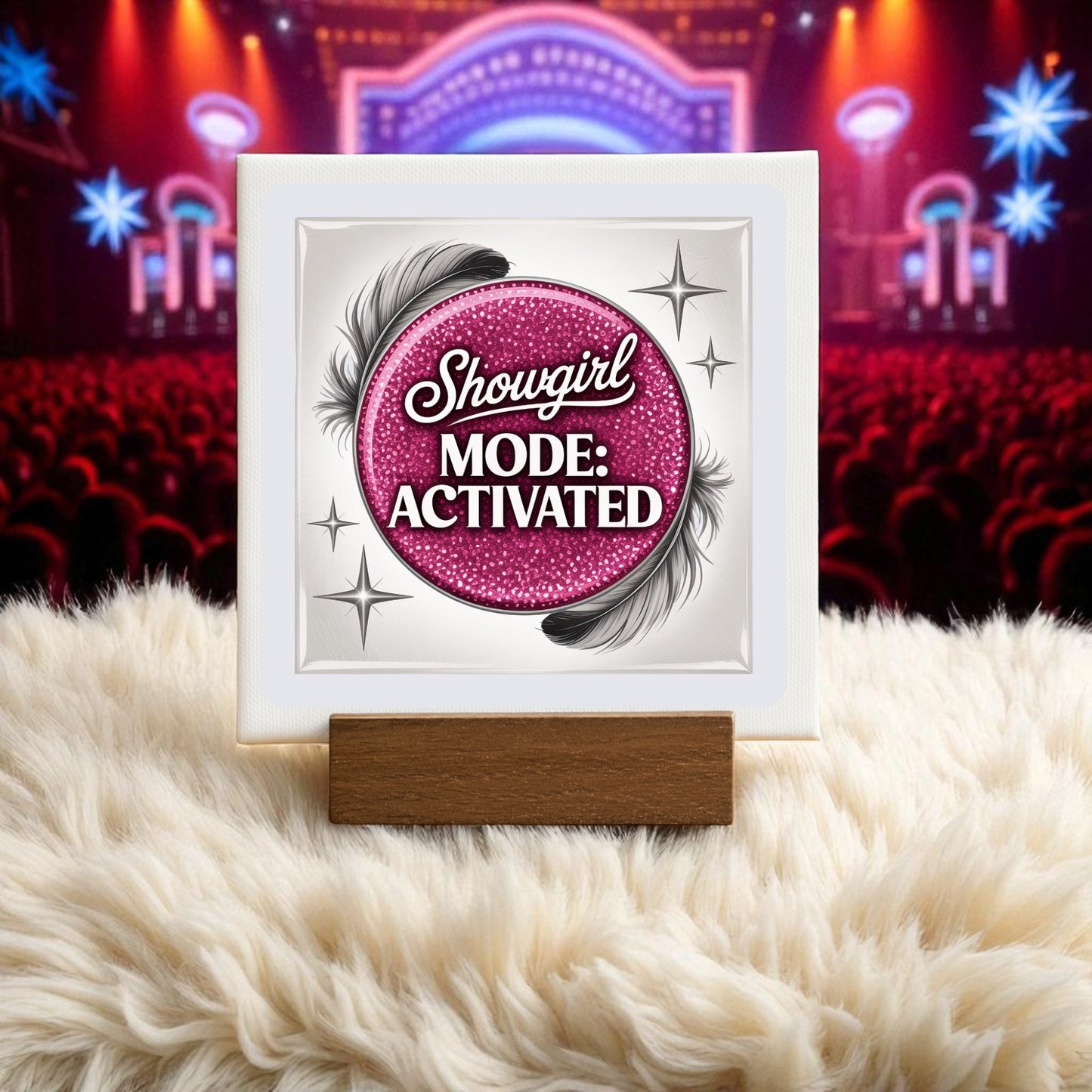 The Showgirl Mode Activated Mini Sign by Mirabilia Boutique, featuring pink glitter, feathers, and stars on a wooden stand, adds glam to any table as chic decor against a blurred theater stage and audience backdrop.