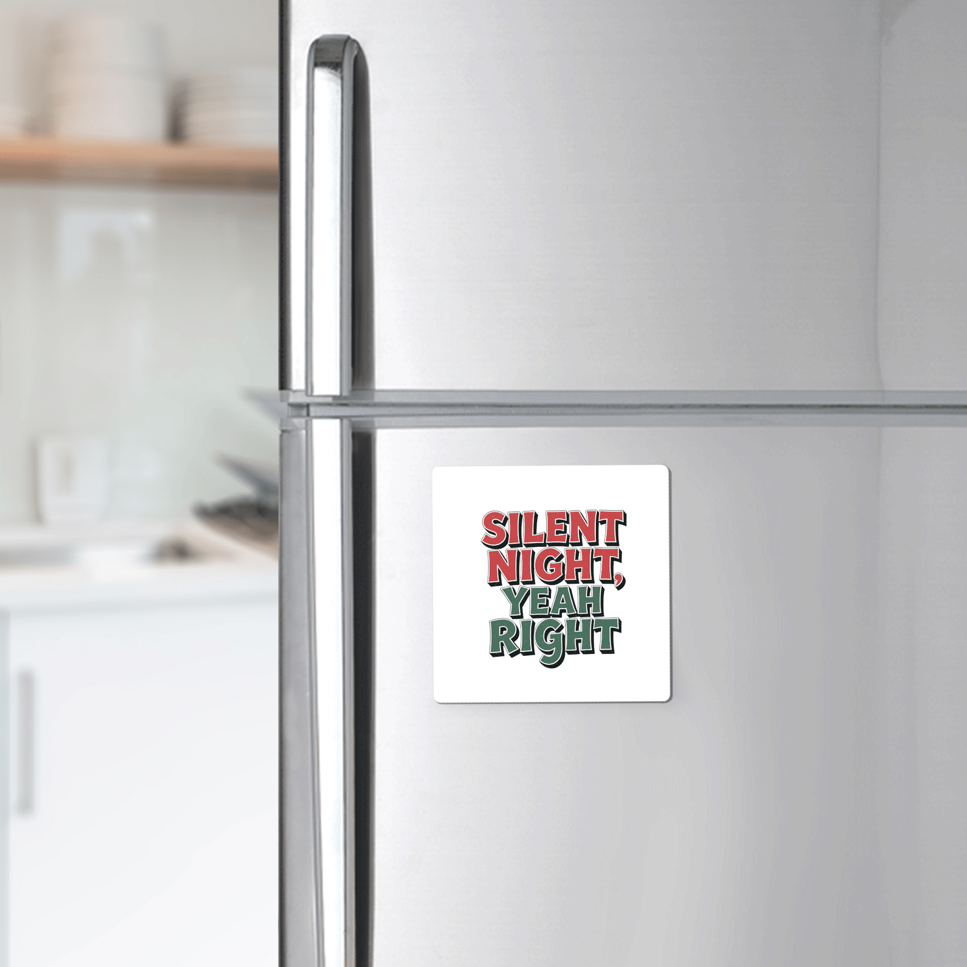 A silver fridge displays the Mirabilia Boutique Silent Night Yeah Right Magnet, a square holiday magnet with red and green text—funny decor for any kitchen or a great stocking stuffer. White shelves and dishes appear in the background.