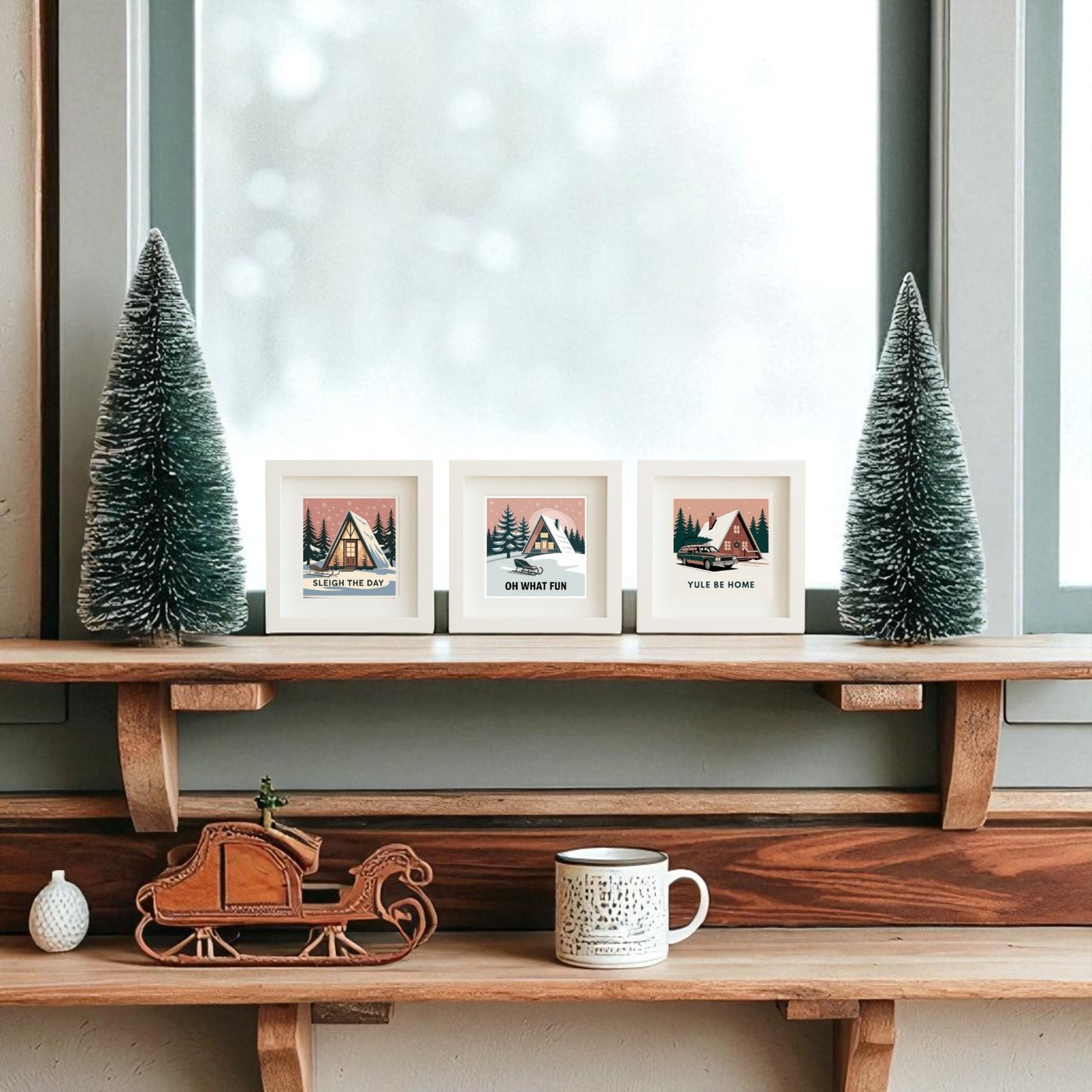 A wooden shelf featuring Mirabilia Boutique’s Mid-Century Modern A-Frame Cabin Sign Trio and Sleigh the Day Set sits by a frosted window, with framed holiday art, pine tree ornaments, a mini sleigh, and a mug in a cozy winter scene.