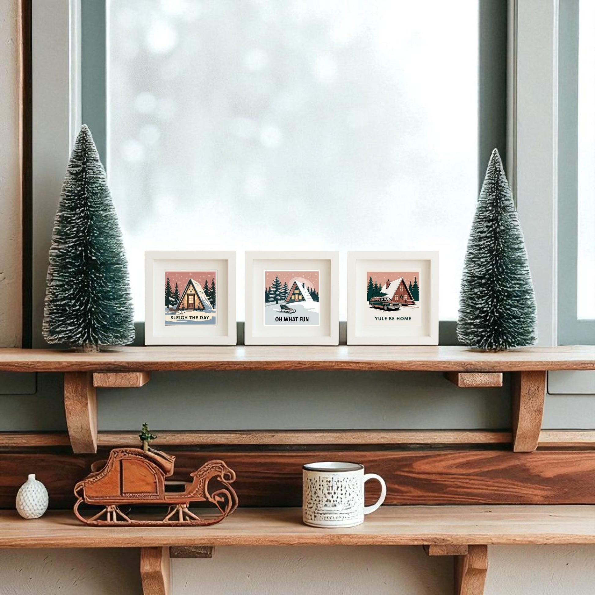 A wooden shelf featuring Mirabilia Boutique’s Mid-Century Modern A-Frame Cabin Sign Trio and Sleigh the Day Set sits by a frosted window, with framed holiday art, pine tree ornaments, a mini sleigh, and a mug in a cozy winter scene.