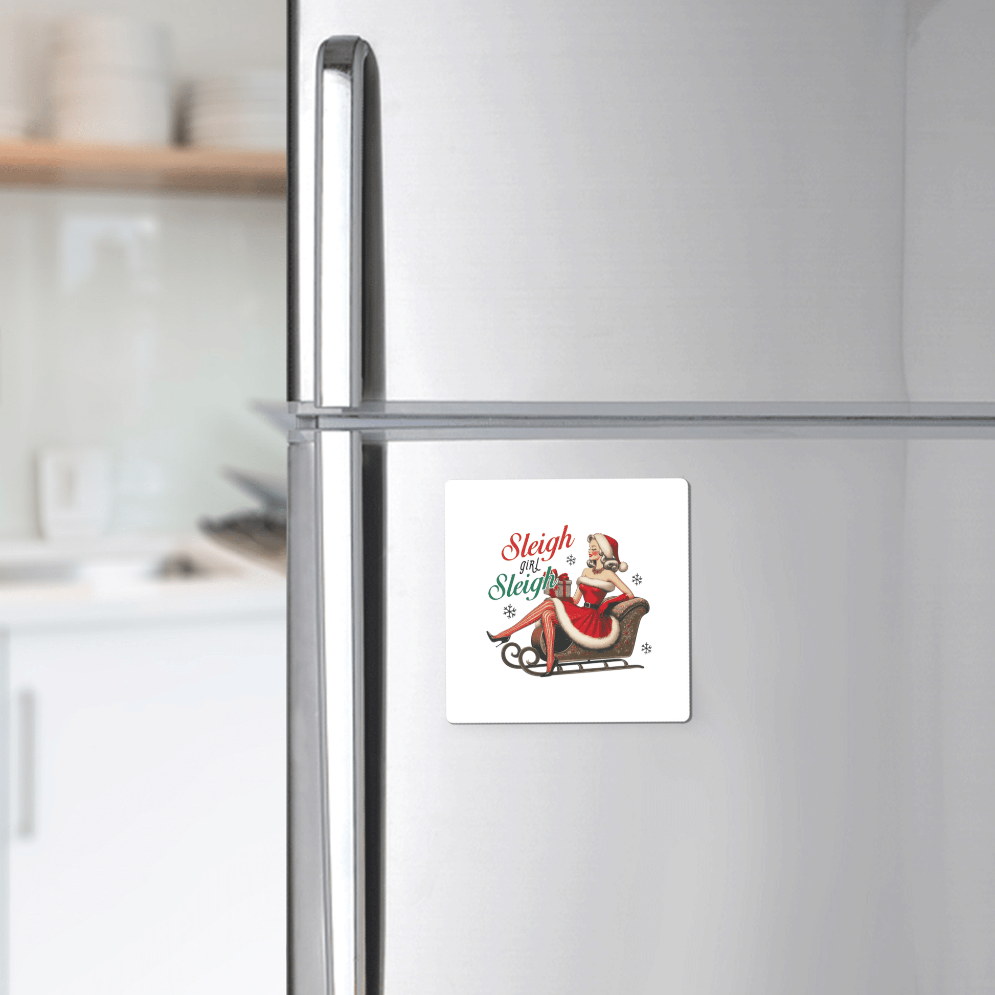 The Sleigh Girl Sleigh Magnet by Mirabilia Boutique is a retro holiday fridge decor featuring a woman in a Santa hat on a sleigh and the text "Sleigh Sleigh Sleigh." Perfect for adding vintage pin-up flair to your festive kitchen!.